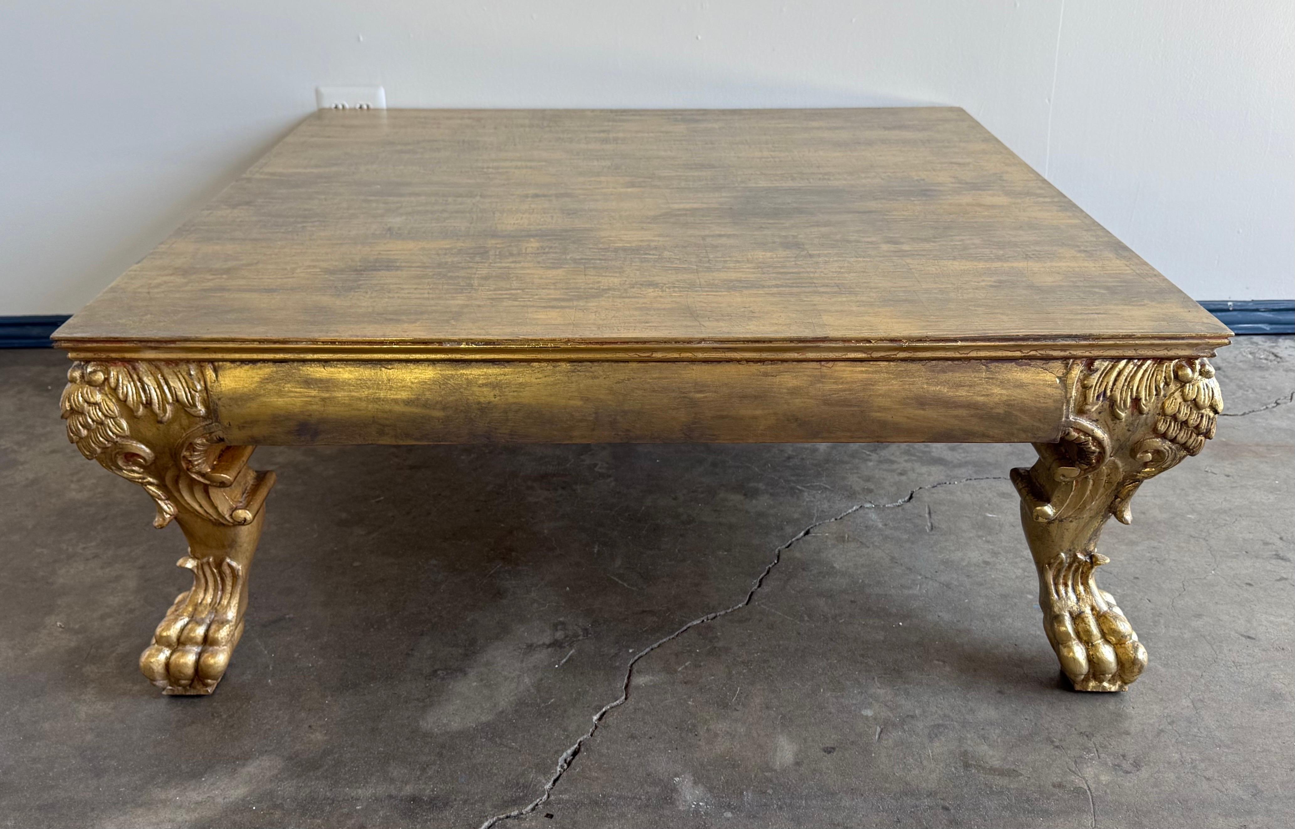 This striking carved wood coffee or low table features a genuine gold leaf finish and is designed in the Baroque style. The square top has a subtle, hand-applied finish that contrasts elegantly with the richly gilded base. The standout elements are