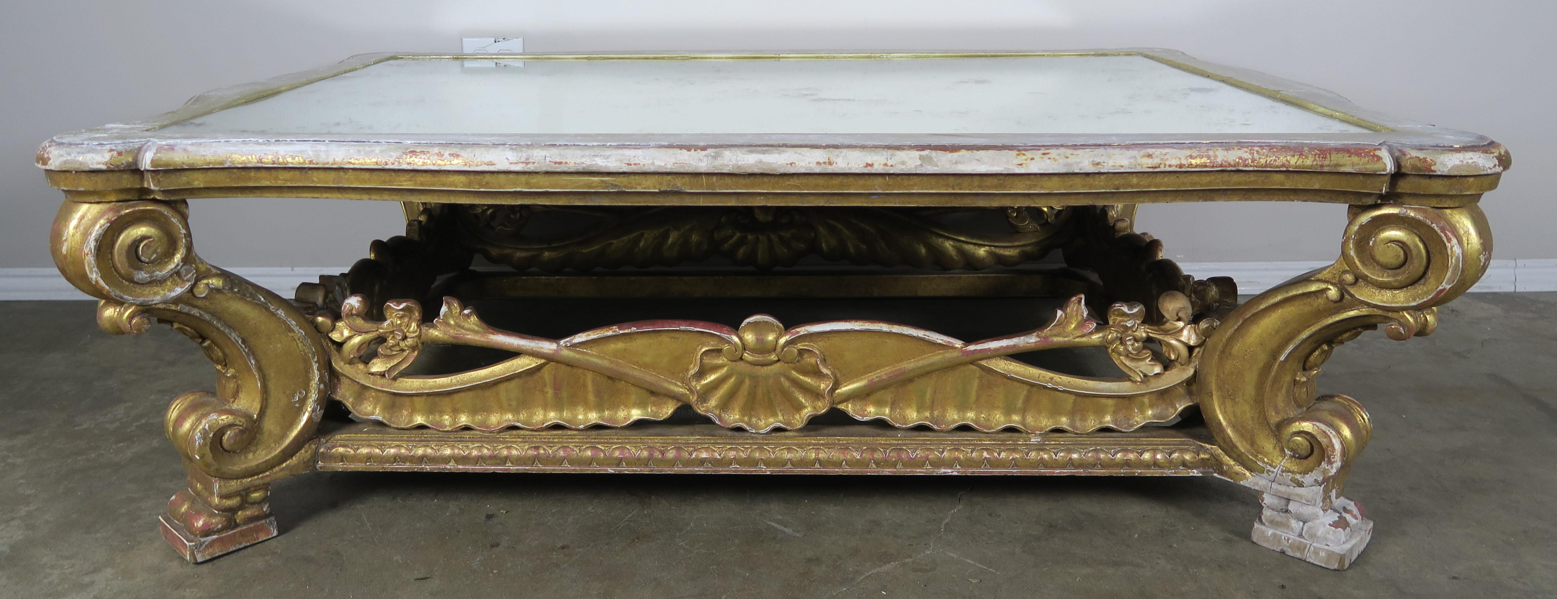 Italian giltwood carved coffee table that stands on four scrolled leg. The legs are connected by carved giltwood panels with a centre shell motif. Antiqued mirror is inset into the top of the table.