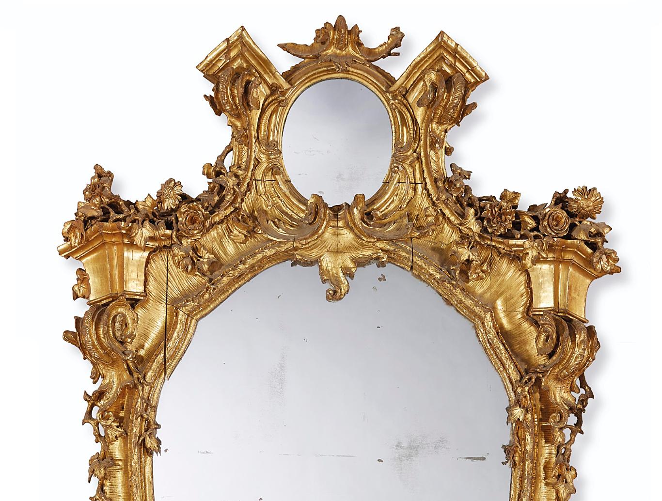 A large 19th century Italian giltwood mirror, the shaped frame carved with garlands of flowers and leaves, on a scallop shell background, with an oval mirror panel to the top flanked by architectural corbels, draped with flowers. Retaining good