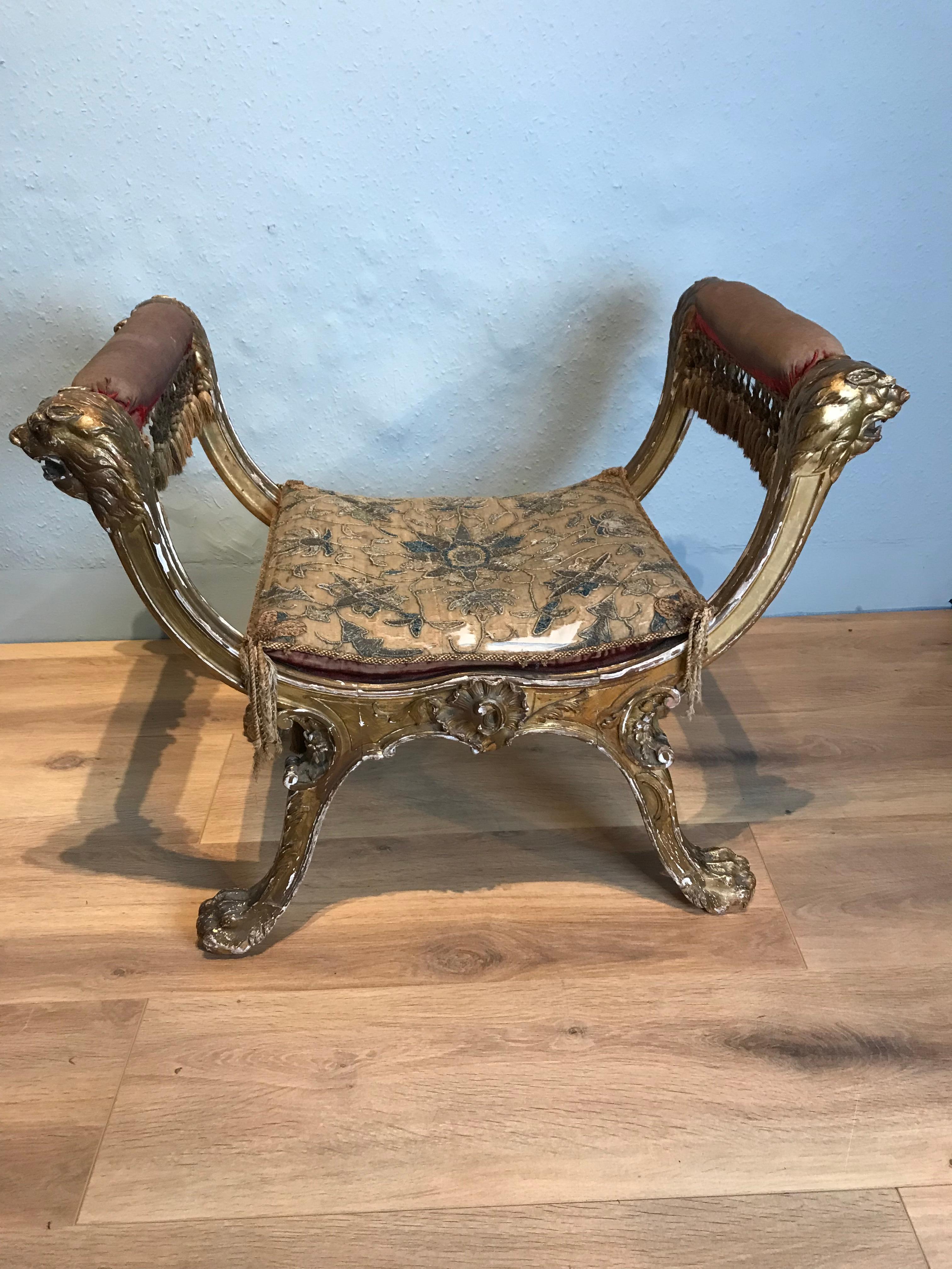 This is a stunning Italian gilt X frame curule stool circa 1800. It features deep bold crisply carved lions heads, paws, corners scrolls and side rails. The gilding is slightly worn but untouched, it retains its original silk seat cushion and