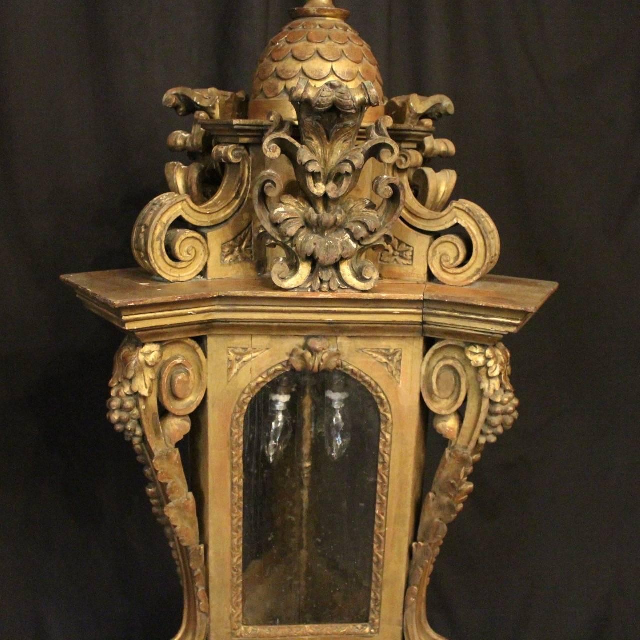 A large Italian carved giltwood triple light antique hall lantern, the mottled shaped glass panels held within an ornate scrolling framework with three internal light fittings and having decorative scrolled central cartouche embellishments, sitting