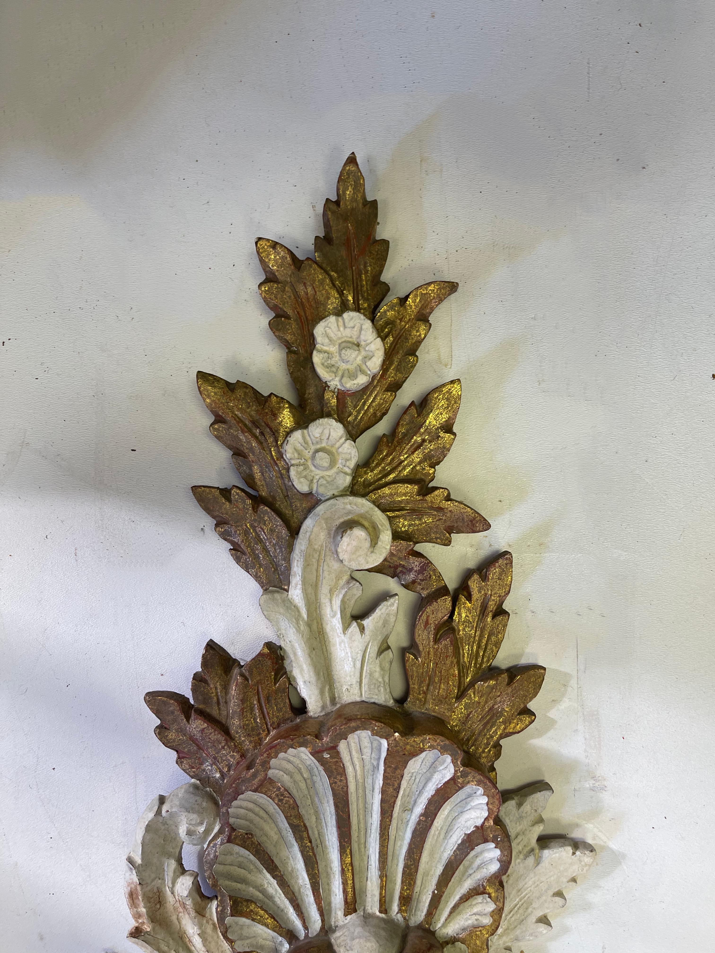 These are lovely and unique. This is a pair of mid-century carved giltwood and ivory painted sconces with an ornate shell and floral motif. They are marked, not electrified and in very good condition.
