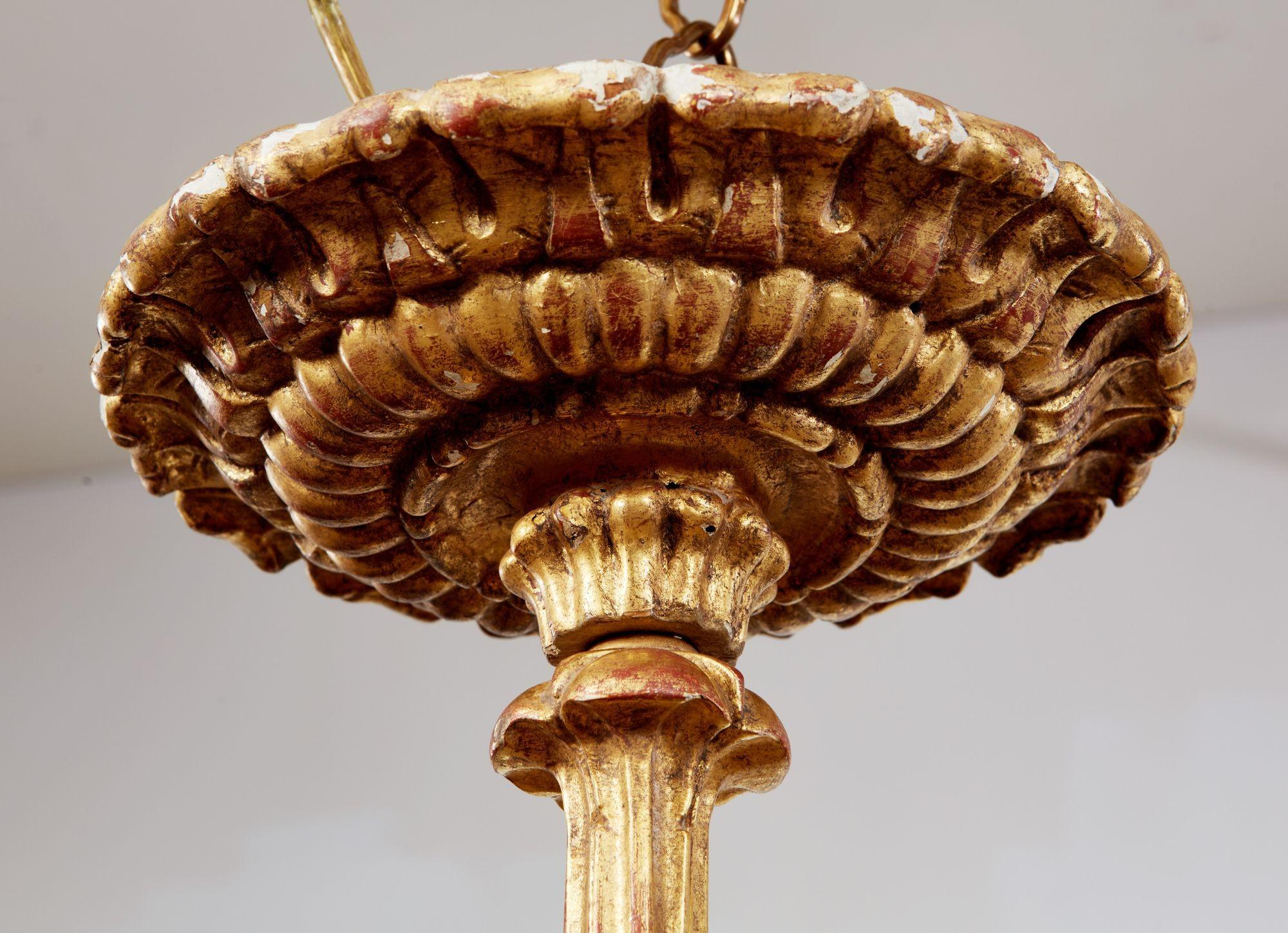 Fine eight light two-tier giltwood chandelier having rose carved pediment, the scroll arms with foliate carving, the central shaft with fluting and floral adornments, all in burnished water gilding having red clay highlights. Italian, mid-19th