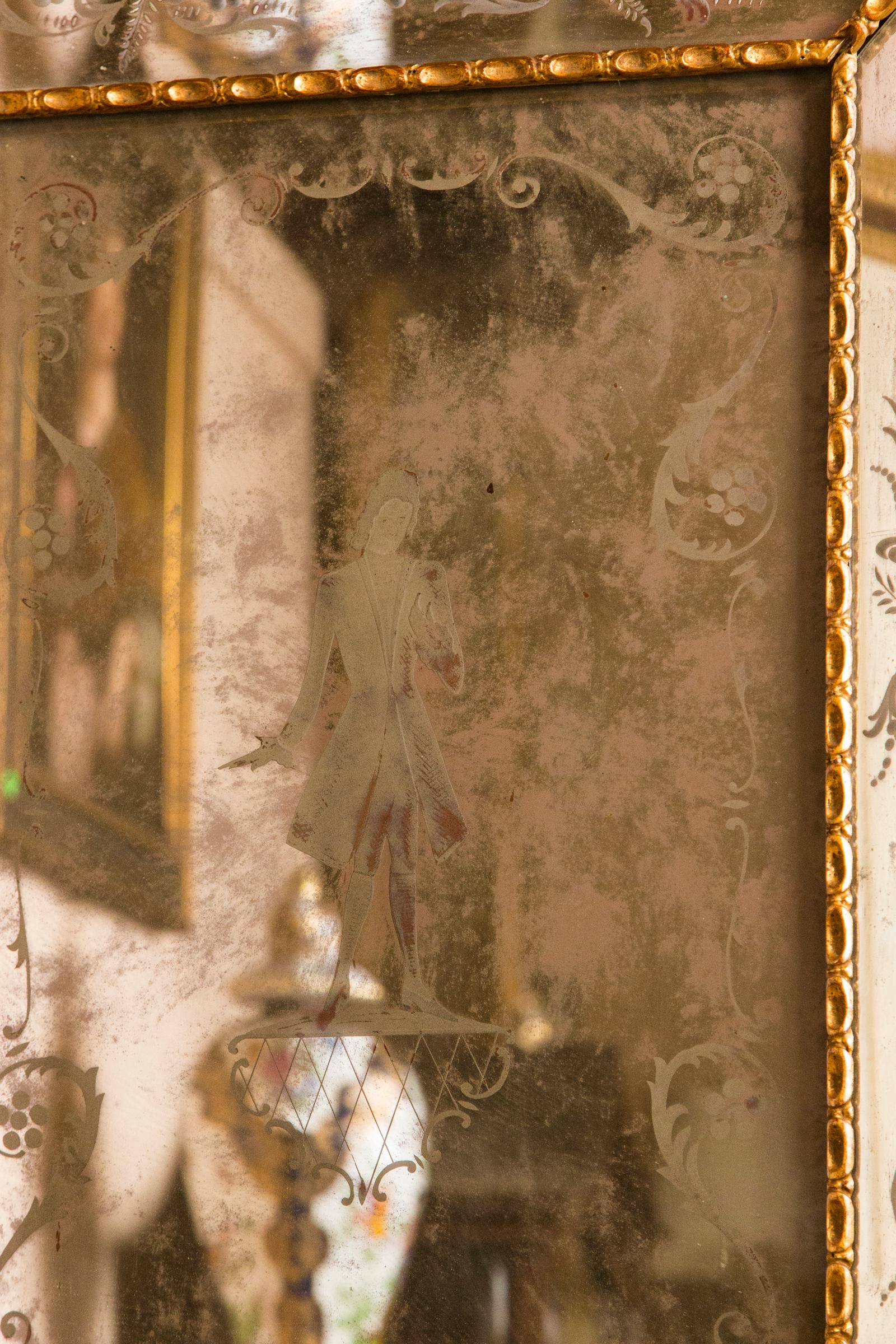 The center glass is etched with a gentleman wearing an open knee length coat. The surrounding panels etched with foliate scrolls. The top crest with plain mirror behind.