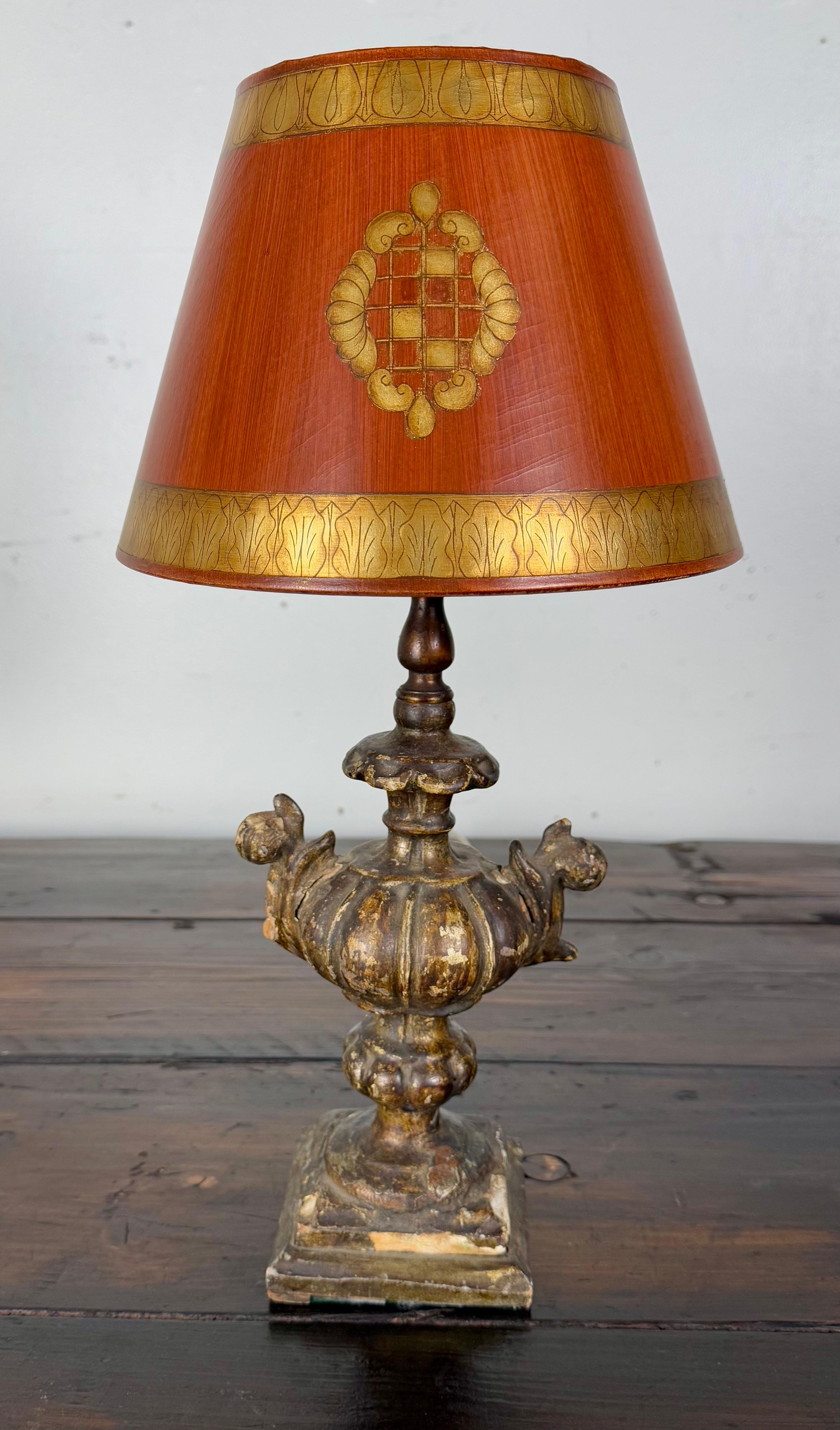 Giltwood urn lamp with an ornate, classical design,  The Rococo inspired base is heavily ornamented with intricate scroll and acanthus leaf motifs, reminiscent of European antiques.  The base has a distressed gold finish, adding to its old-world