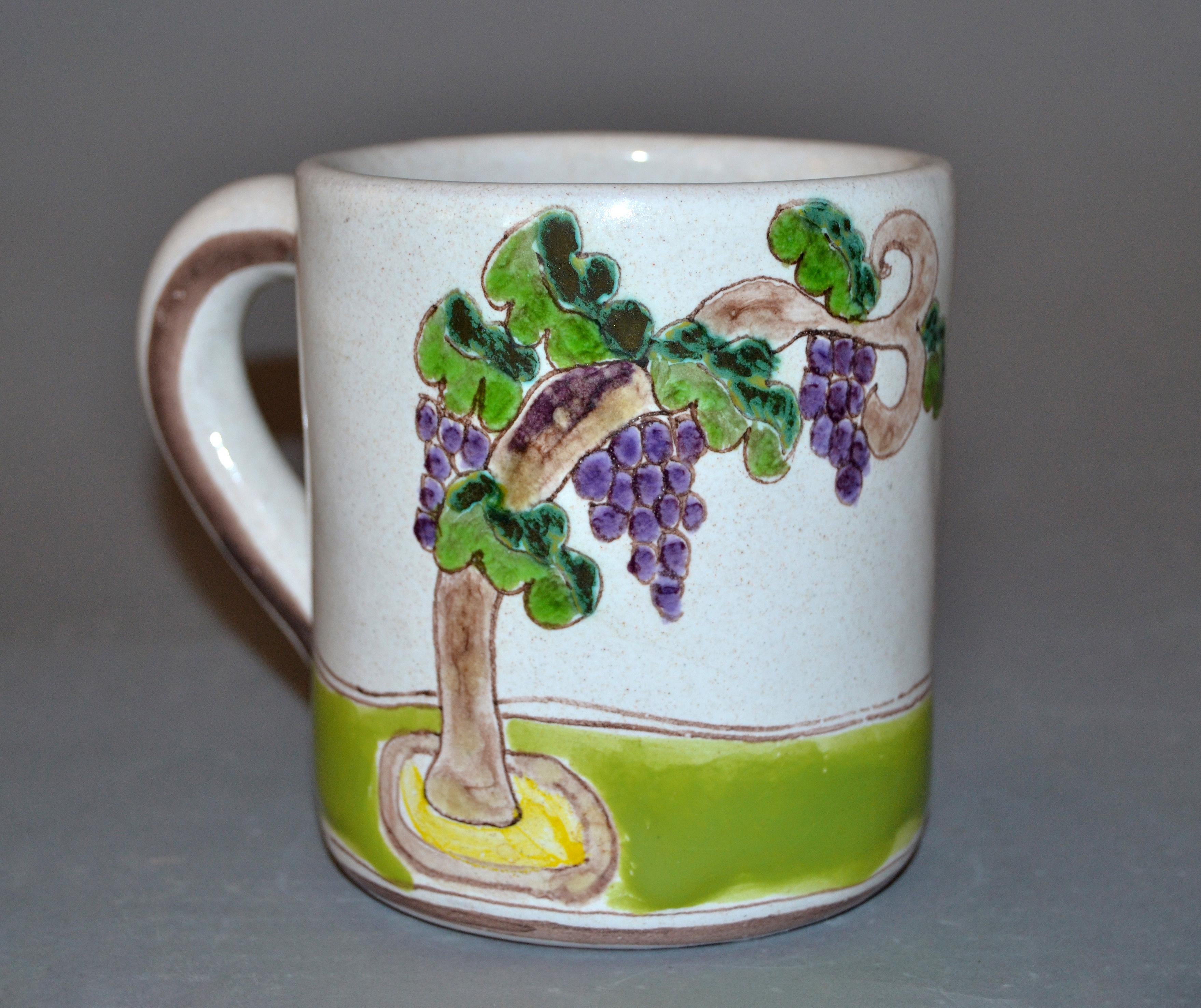 Original Italian Giovanni Desimone hand painted art pottery, decor mug or cup with a scene of grapes on the vine and a grape picker.
The mug is glazed and very colorful.
Makers Mark and numbered on underside, 'Desimone, Italy 102/3'.
 