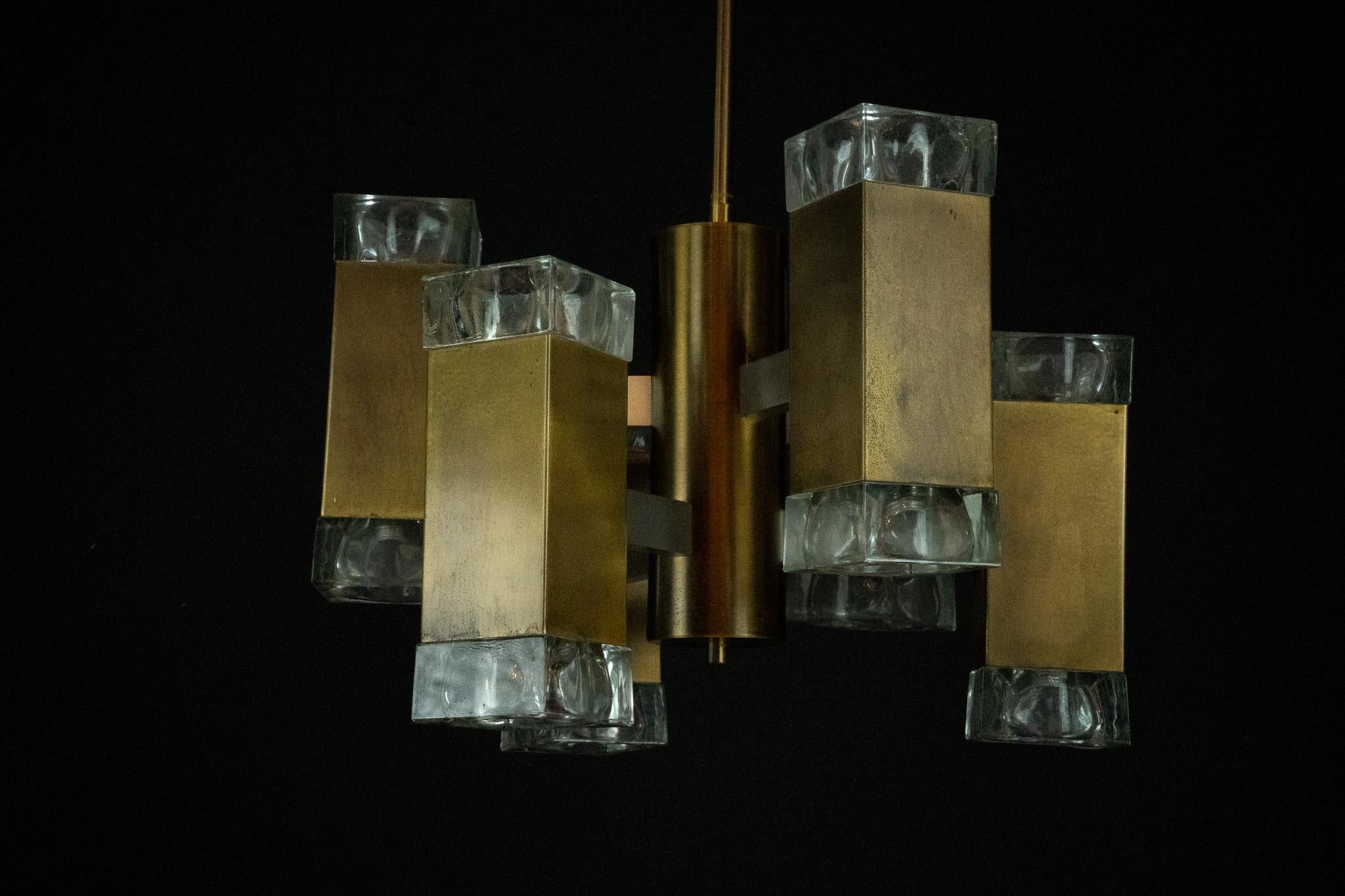Lustre italien à 12 lumières en laiton et verre, produit par Gaetano Sciolari dans les années 1970. Le design présente une tige centrale en laiton avec des bras géométriques, chacun équipé d'un abat-jour cubique en verre clair aux deux extrémités,