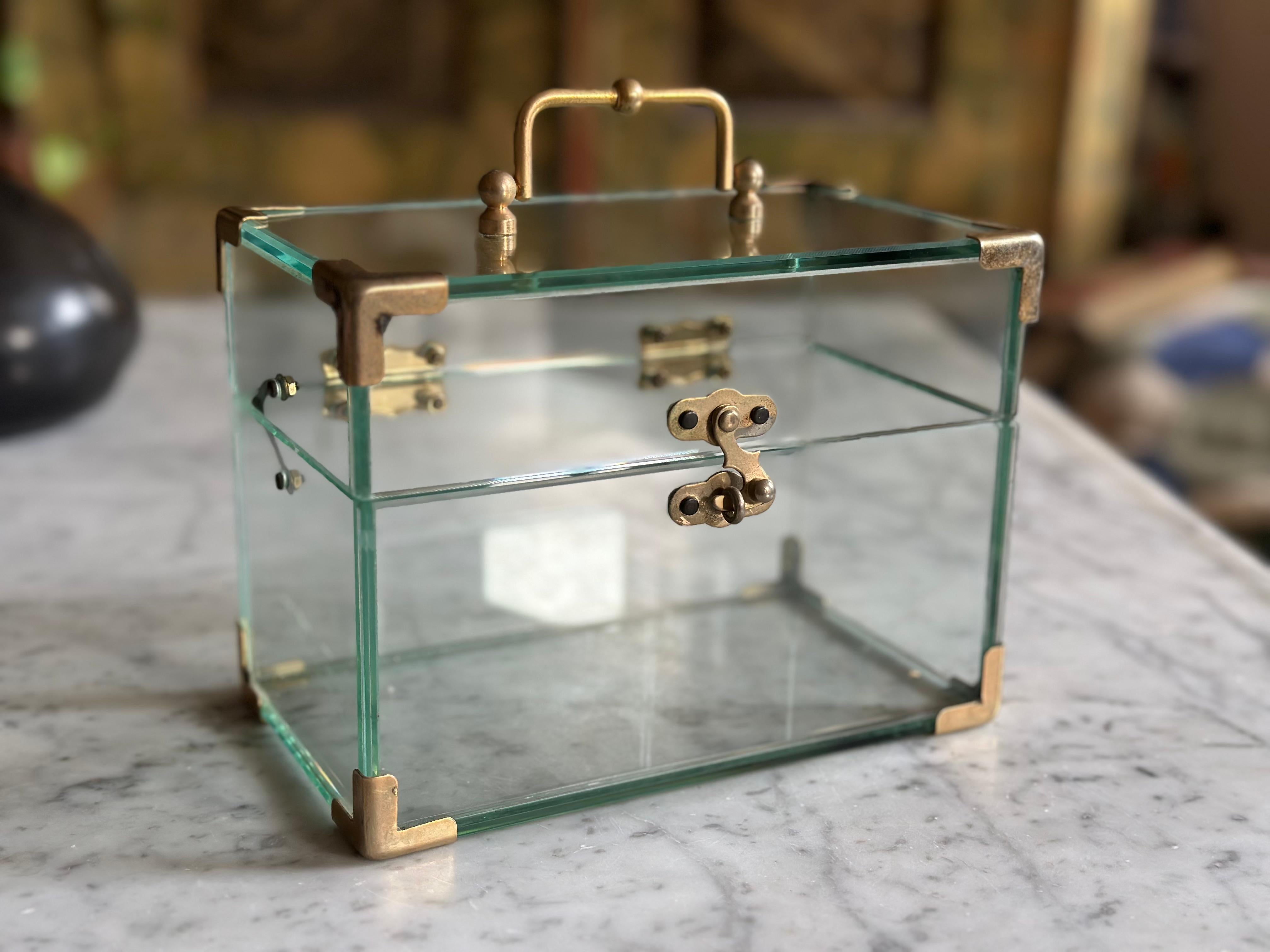 Dieses bezaubernde Glaskästchen mit vergoldeten Metallbeschlägen und einem zierlichen Griff erinnert sofort an die Form eines Miniaturkoffers. Das in den 1970er Jahren in Italien hergestellte Dekorationsobjekt spiegelt den Glamour und die verspielte