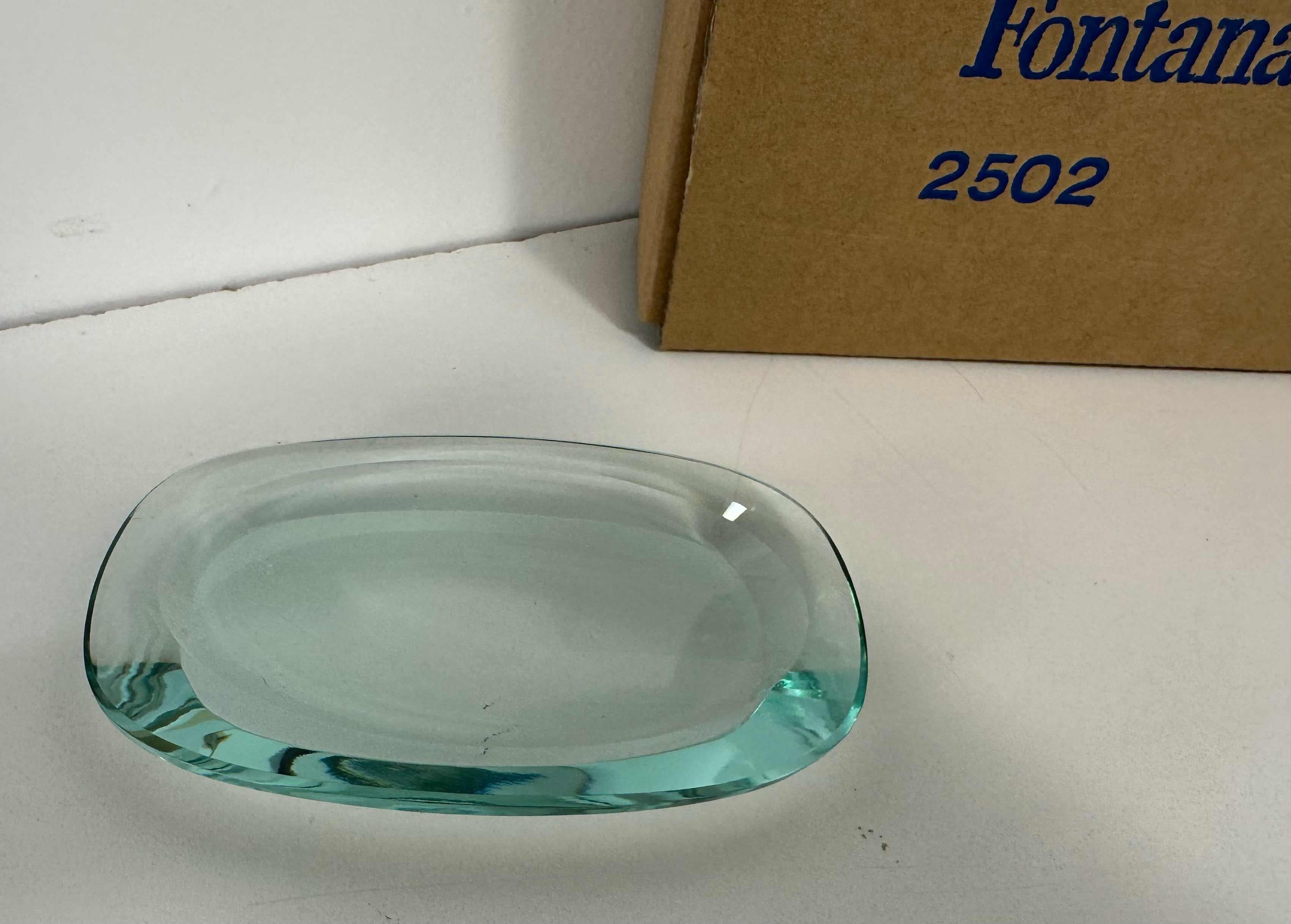 Gracieux cendrier de Fontana Arte produit en Italie vers les années 60/70. Conserver la boîte d'origine. Modèle 2502.

En très bon état Vintage By.

Dimensions du cendrier : 14cm x 9cm H2cm

Dimensions de la boîte : 20cm x 7cm H14cm