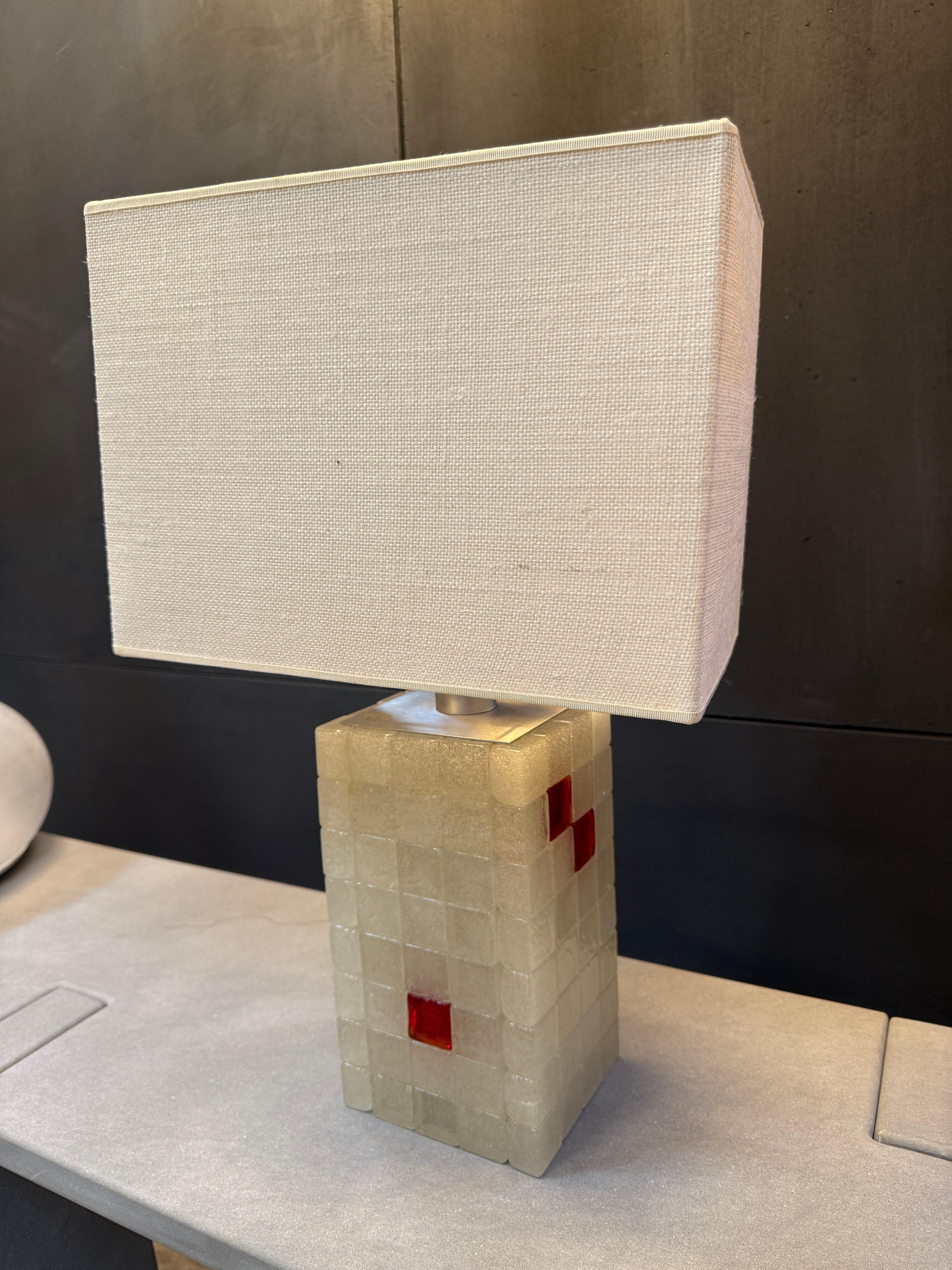 An architectural Italian table lamp from the 1970s, featuring a geometric glass block base with textured surfaces and inset ruby-red accents. The squared, grid-like structure gives the piece a sculptural quality, while the pops of red add a bold,