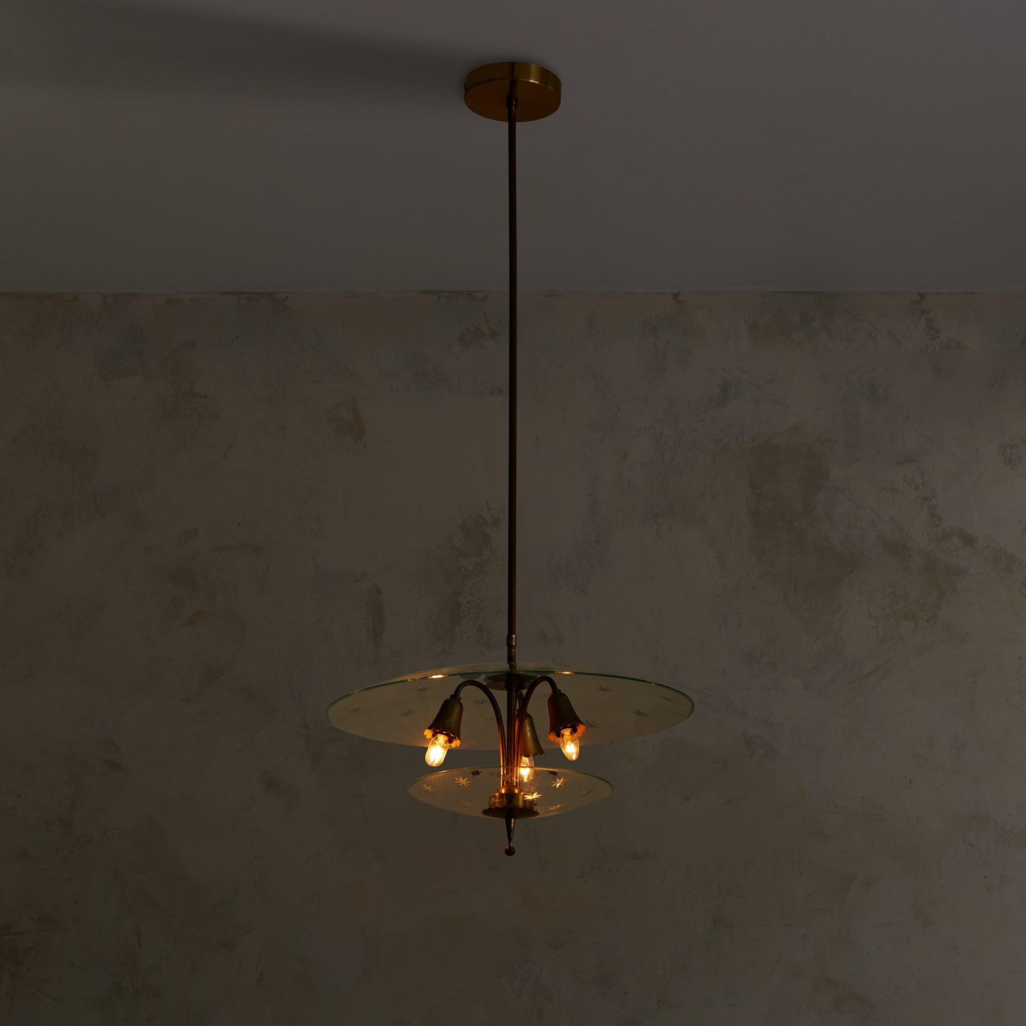 Composición lírica en cristal y latón, esta lámpara de los años 40 se atribuye a Pietro Chiesa para Fontana Arte. Suspendidos de un delgado vástago de latón, dos discos flotantes de cristal con motivos de estrellas grabadas enmarcan un trío de