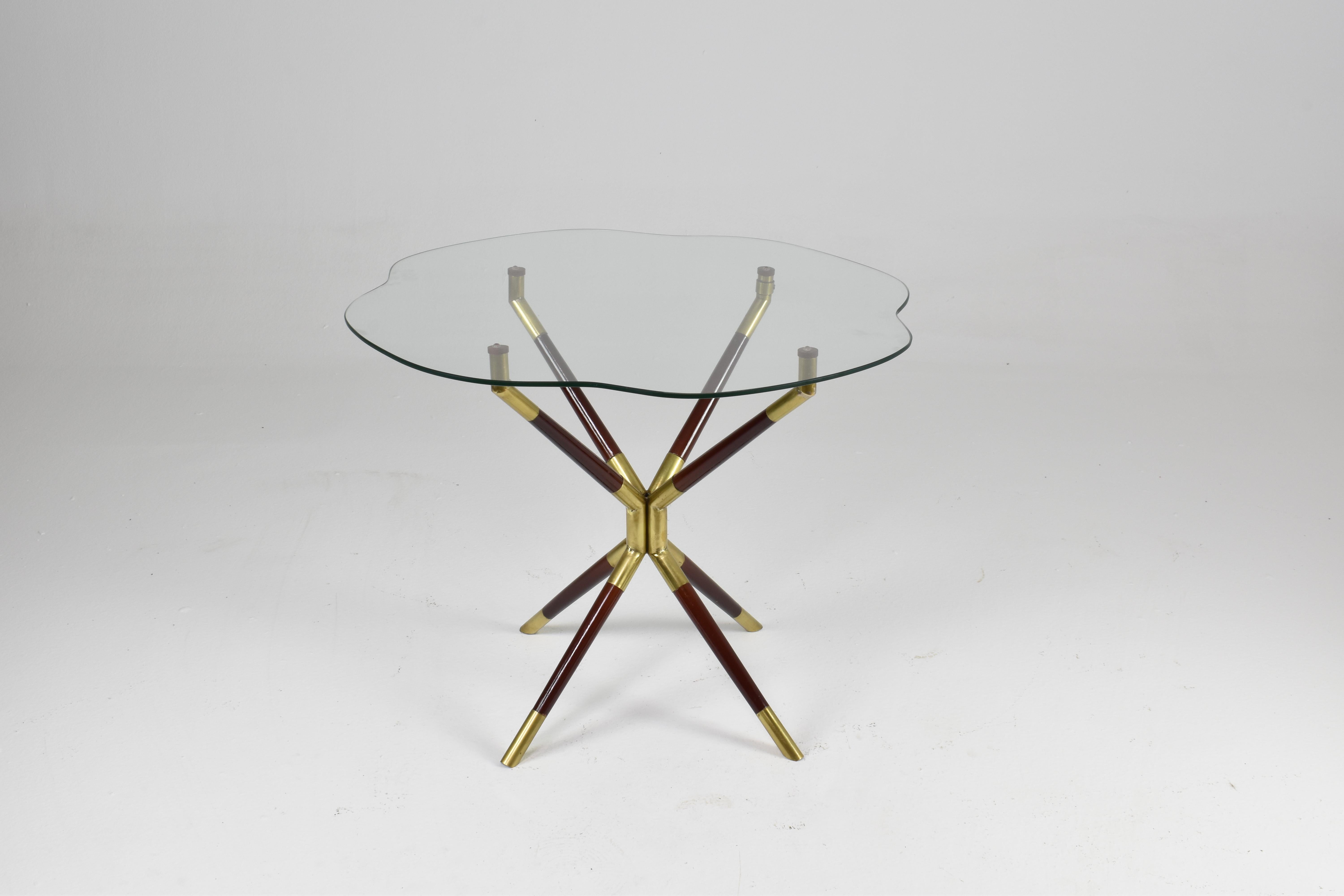 A 1950s Italian mid-century modern coffee table attributed to Cesare Lacca. Its organic, petal-shaped glass top rests on a sculptural base of four splayed lacquered metal legs, each connected with polished brass endings. The central brass structure