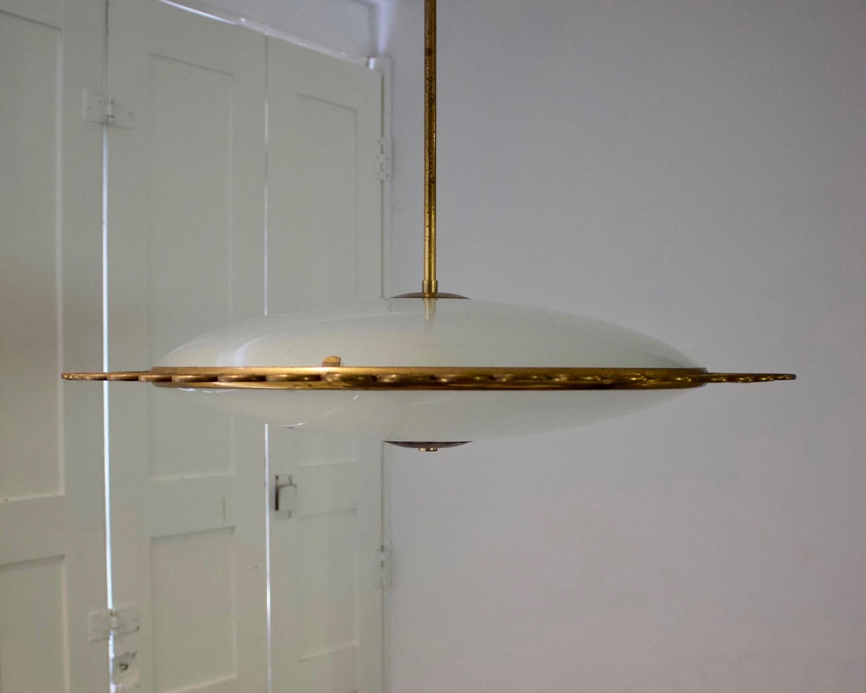 Italian glass pendant light with decorative brass frame, mid-20th century. 

A delicate fixture made up of two dishes of opaque glass held by a decorative brass frame. The slim flying saucer shape is very much in the style of Pietro Chiesa for