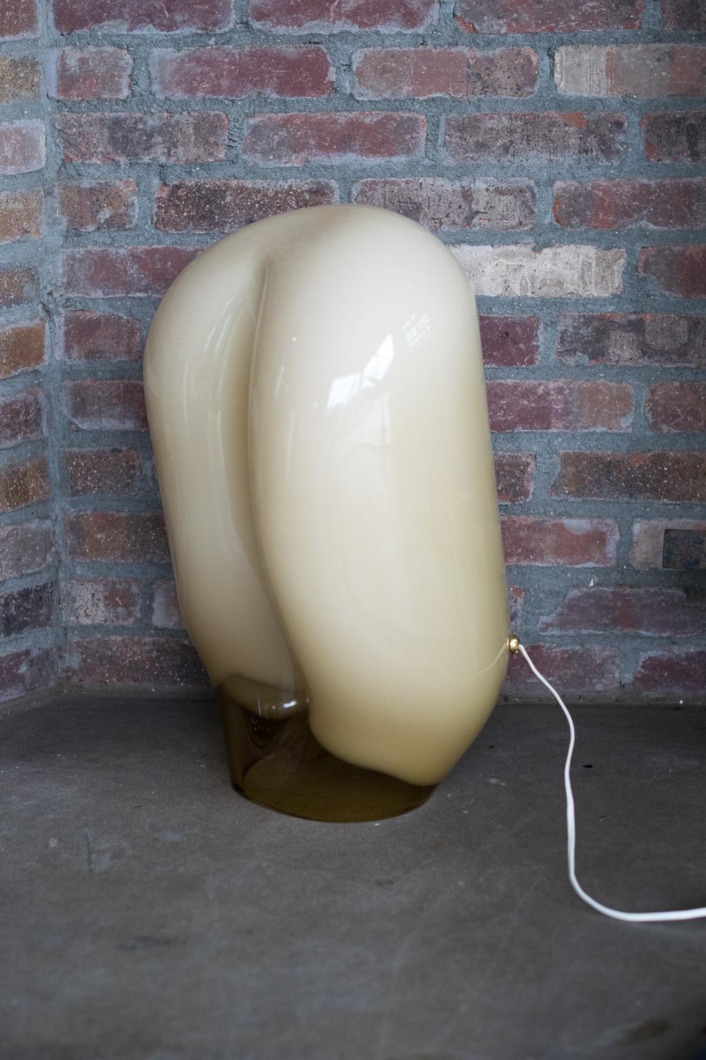 Sculptural Murano glass table lamp, designed by Gino Vistosi. Amorphic in form, color fades from opaque buff or beige to clear amber glass. Emits a warm white light when lit. Late Mid-Century Modern to modern styling. One large and one small