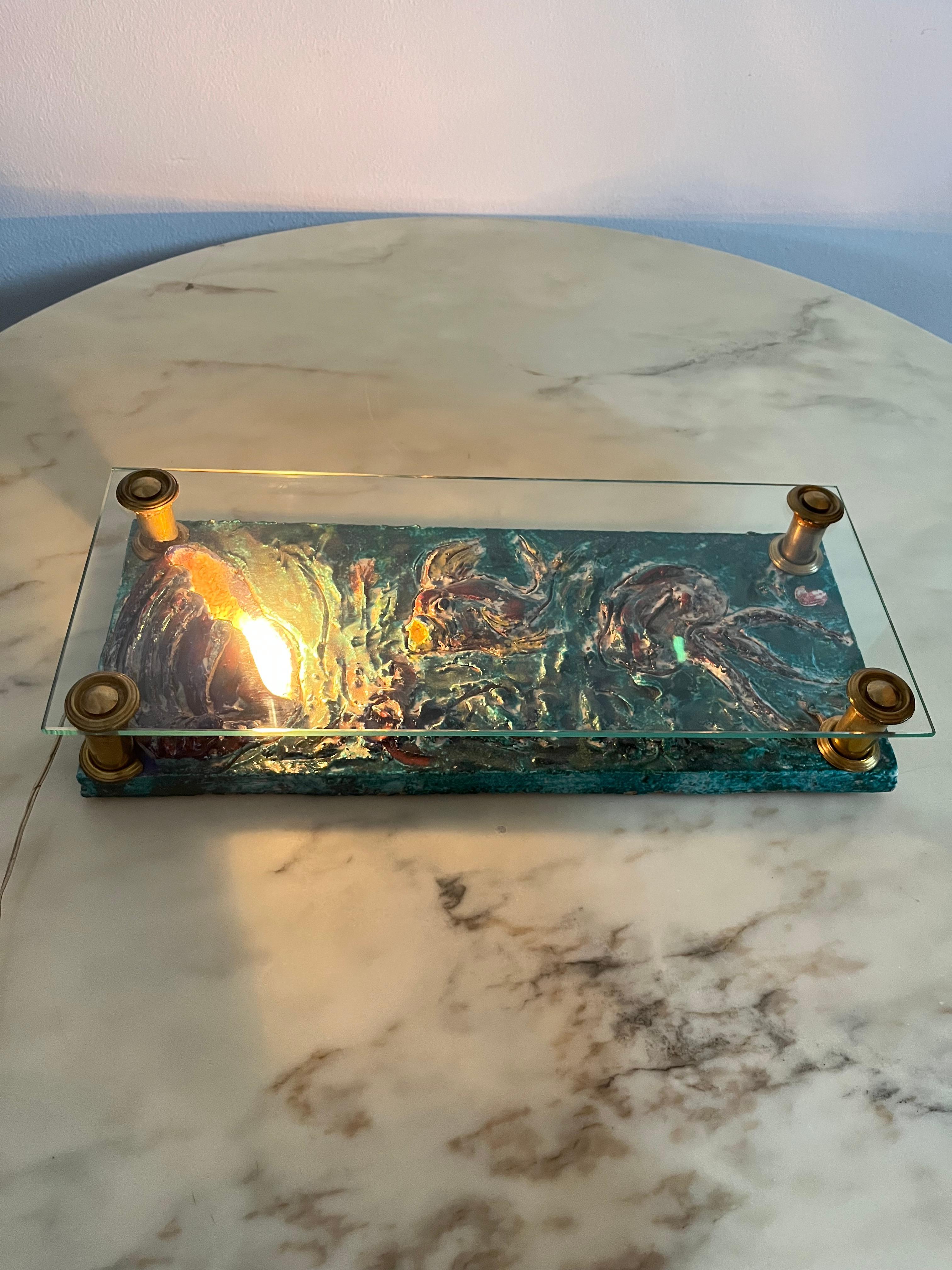 Italian glazed terracotta table lamp, 1950s
Depicted a seascape with fish and shells.
Glass top and brass supports. Single piece.
Small signs of time and use, as evidenced by the photographs of the description.