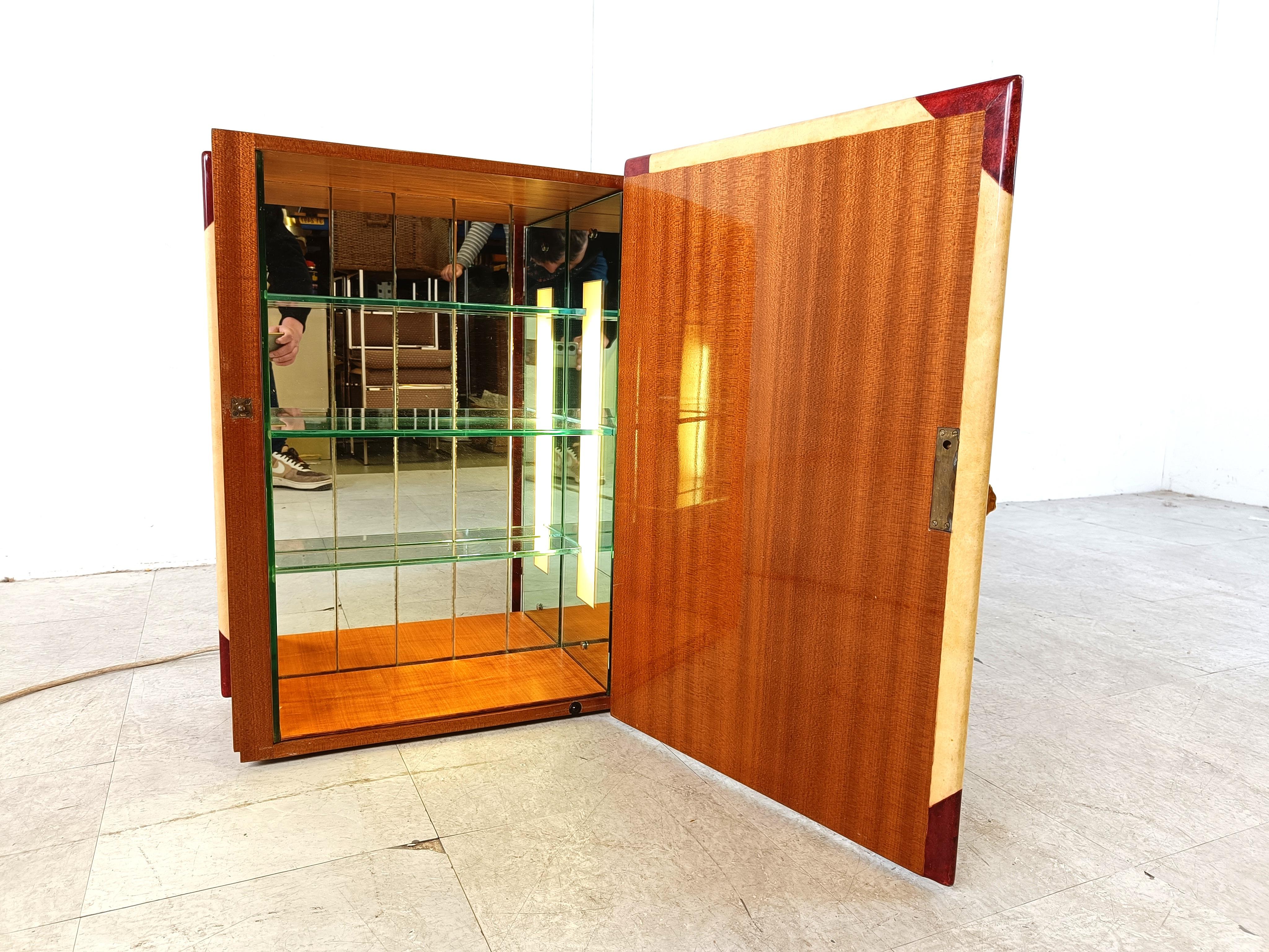 Very rare book shaped dry bar cabinet by Aldo Tura.

The cabinet is made from wood, covered in brown and beiige lacquered goatskin with a hand painted renaissance scene and gilt metal hardware.

Inside we find 3 glass shelves and an illuminated