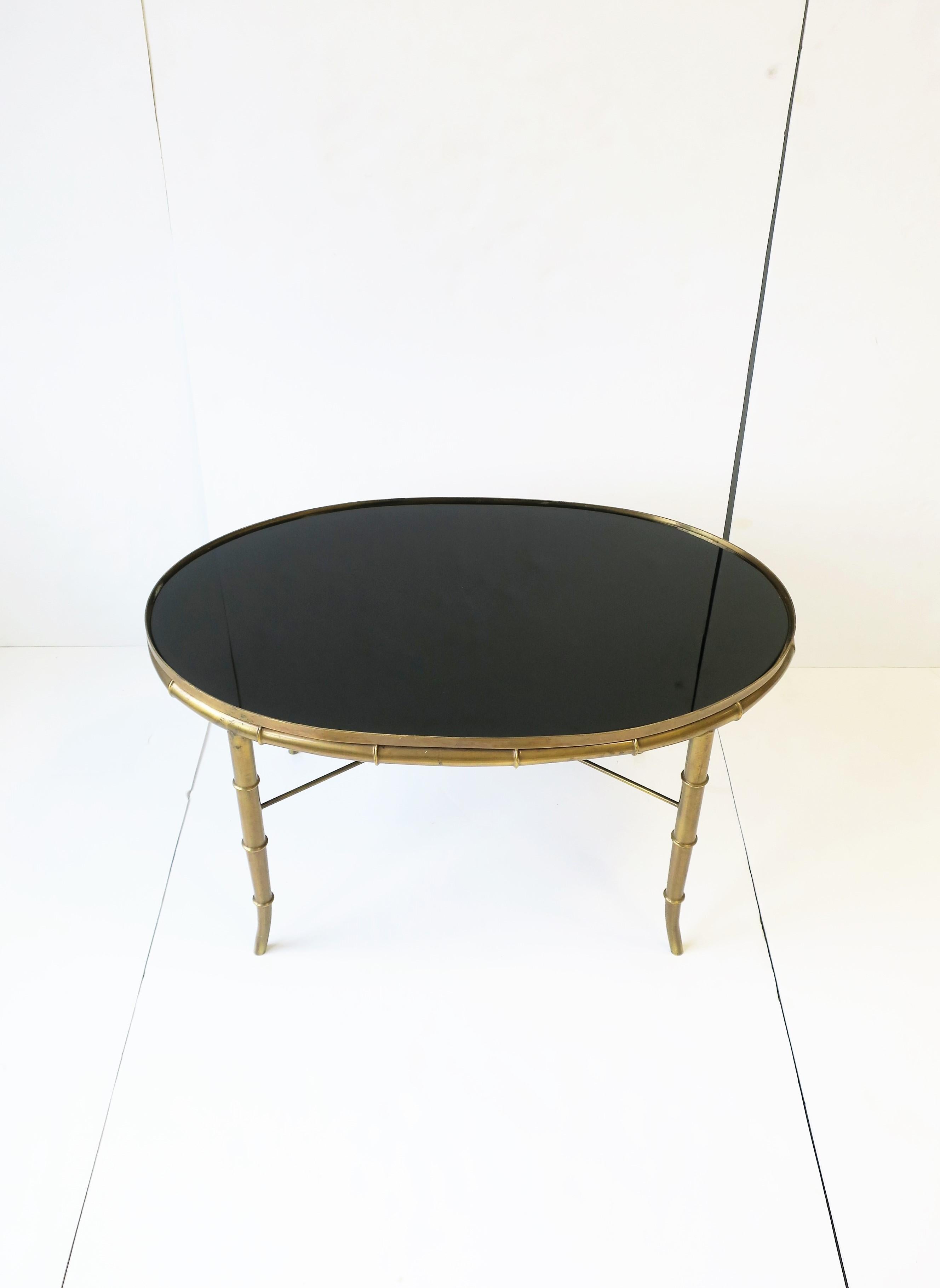 A beautiful Italian oval brass cocktail/coffee table with a brass bamboo-esque frame, circa mid-20th century, 1960s to early 1970s, Italy. Brass frame is a 'bamboo' style, has an 'X' stretcher base, finished with a custom inset oval black glass top.