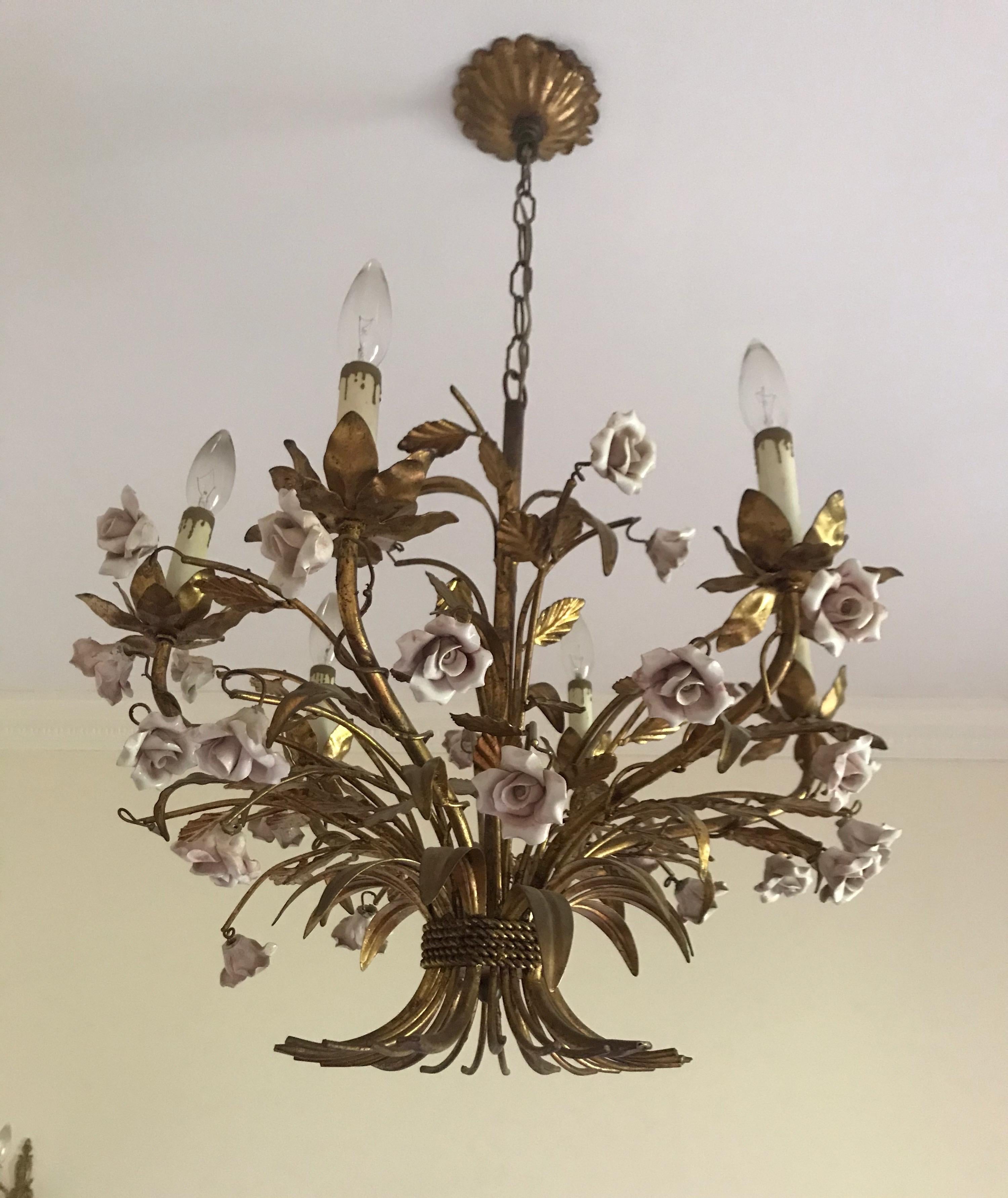 This stunning Italian gold gilt chandelier has a wheat shape shaft and the bottom flairs out with rope wrapped around. It has many gold leaves with beautiful soft pink porcelain roses. The original fluted canopy and chain are included and completes