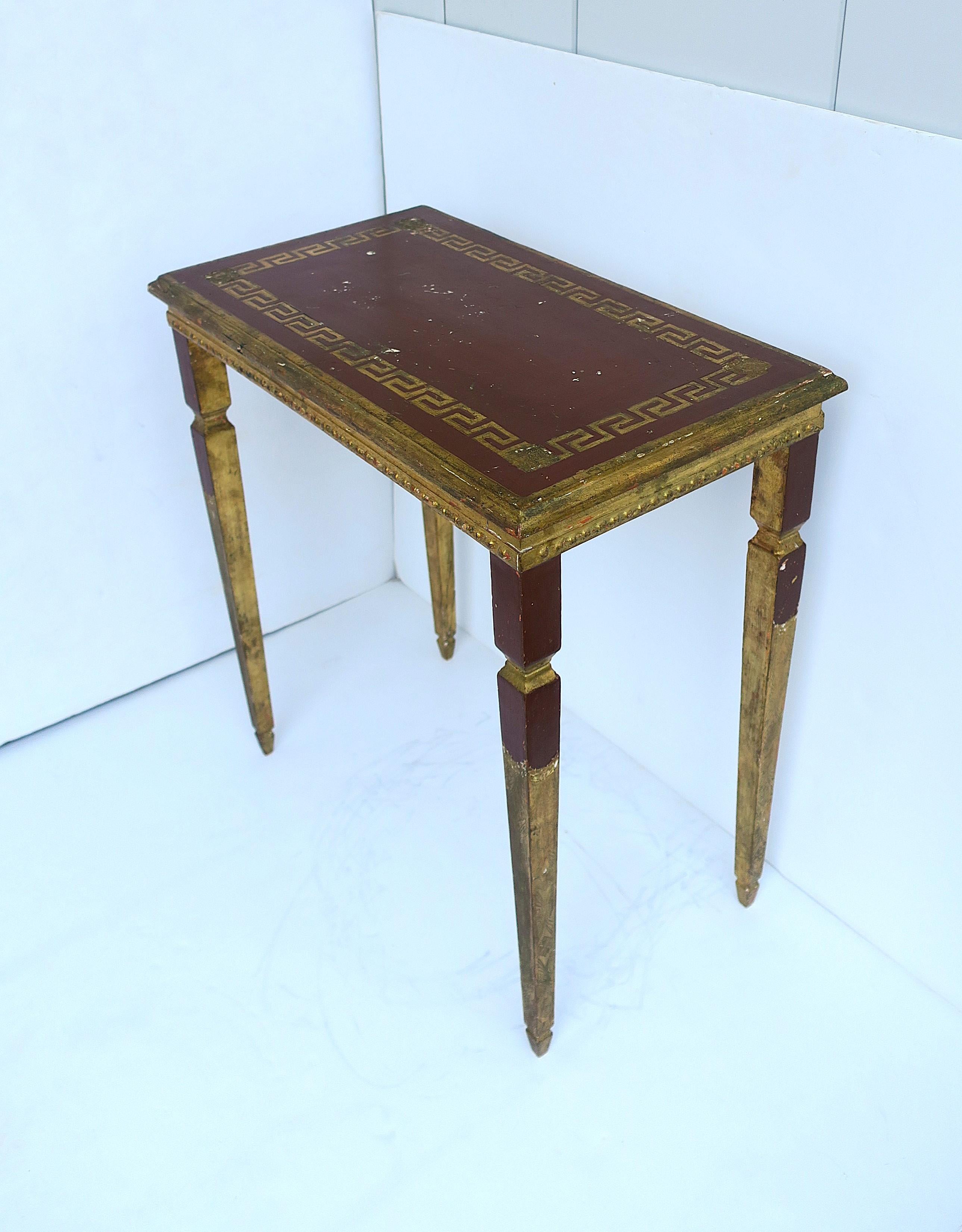 An Italian rectangular gold giltwood side, end, or accent table with Greek-Key design, circa early-20th century, Italy. Table has a red burgundy/terracotta hue on top and legs, decorated with a gold Greek-Key design on tables' top, finished with