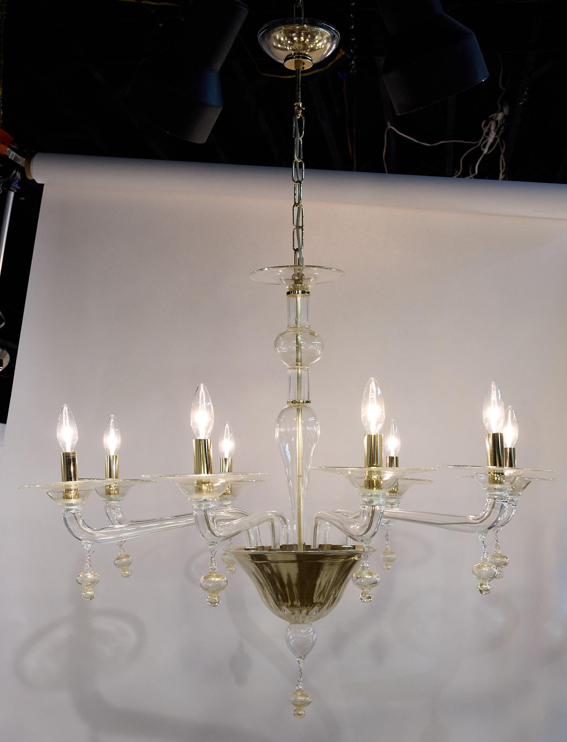 Sleek and elegant 20th Century Murano glass chandelier having eight arms supporting brass candleabras. The fixture is made of clear glass, gold specked glass, and brass accents. 

A matching canopy and gold chain are included and measure an