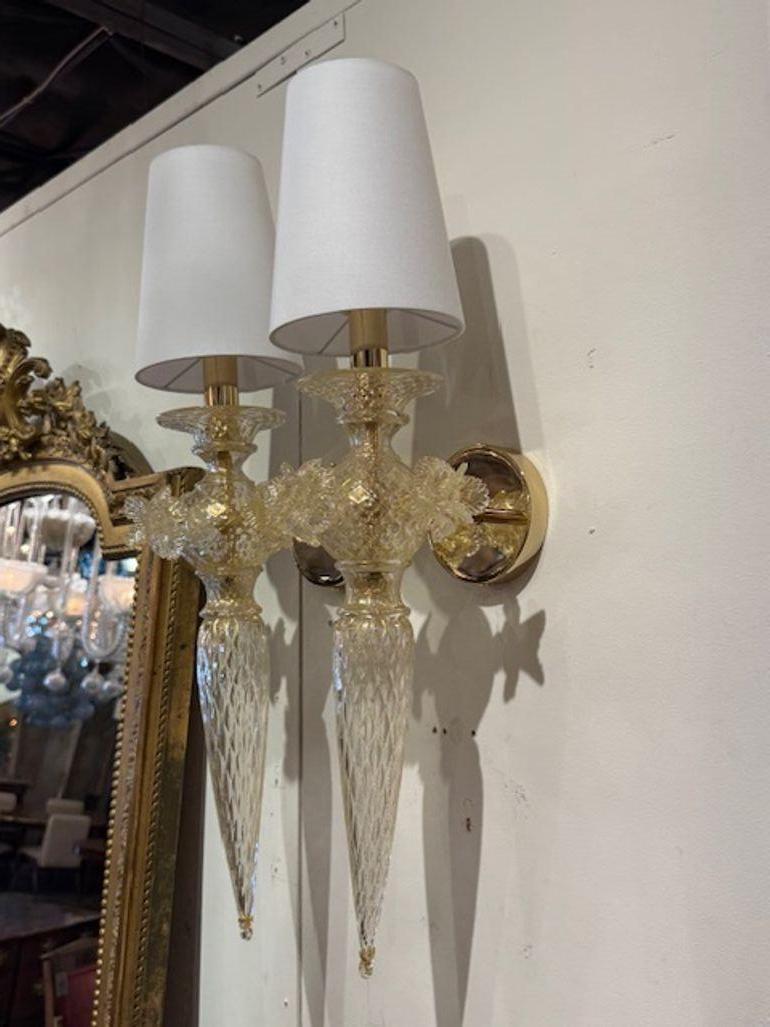 Ces appliques florales italiennes en verre Murano doré sont des luminaires muraux exquis qui ajoutent une touche d'élégance à n'importe quelle pièce. Les abat-jour complexes en forme de fleur sont fabriqués en verre de Murano de haute qualité, ce