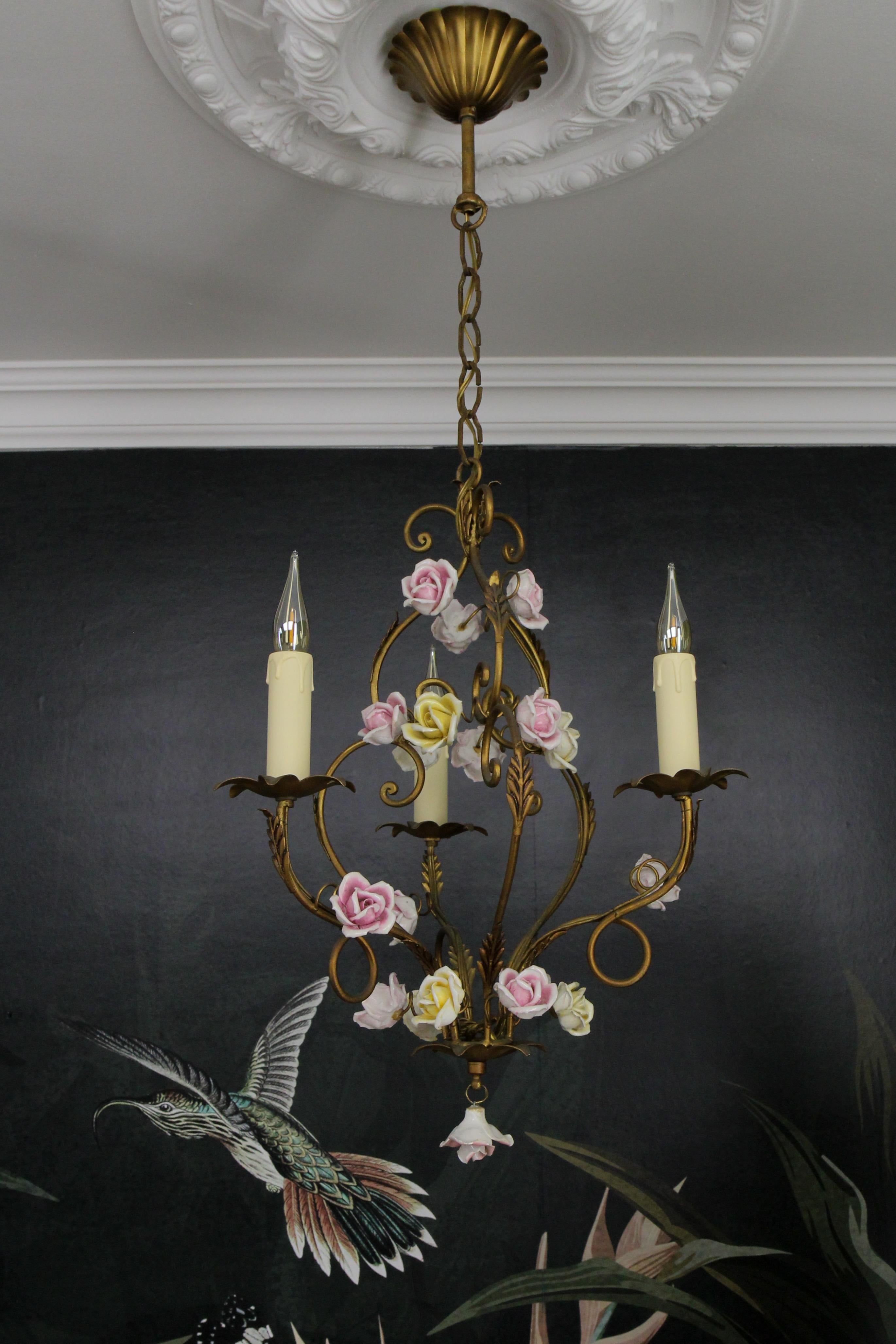 Italian golden color metal and porcelain flower three-light chandelier from the circa 1970s.
This adorable Hollywood Regency-style chandelier features three chandelier arms each with a socket for an E14-size light bulb. The beautifully shaped golden