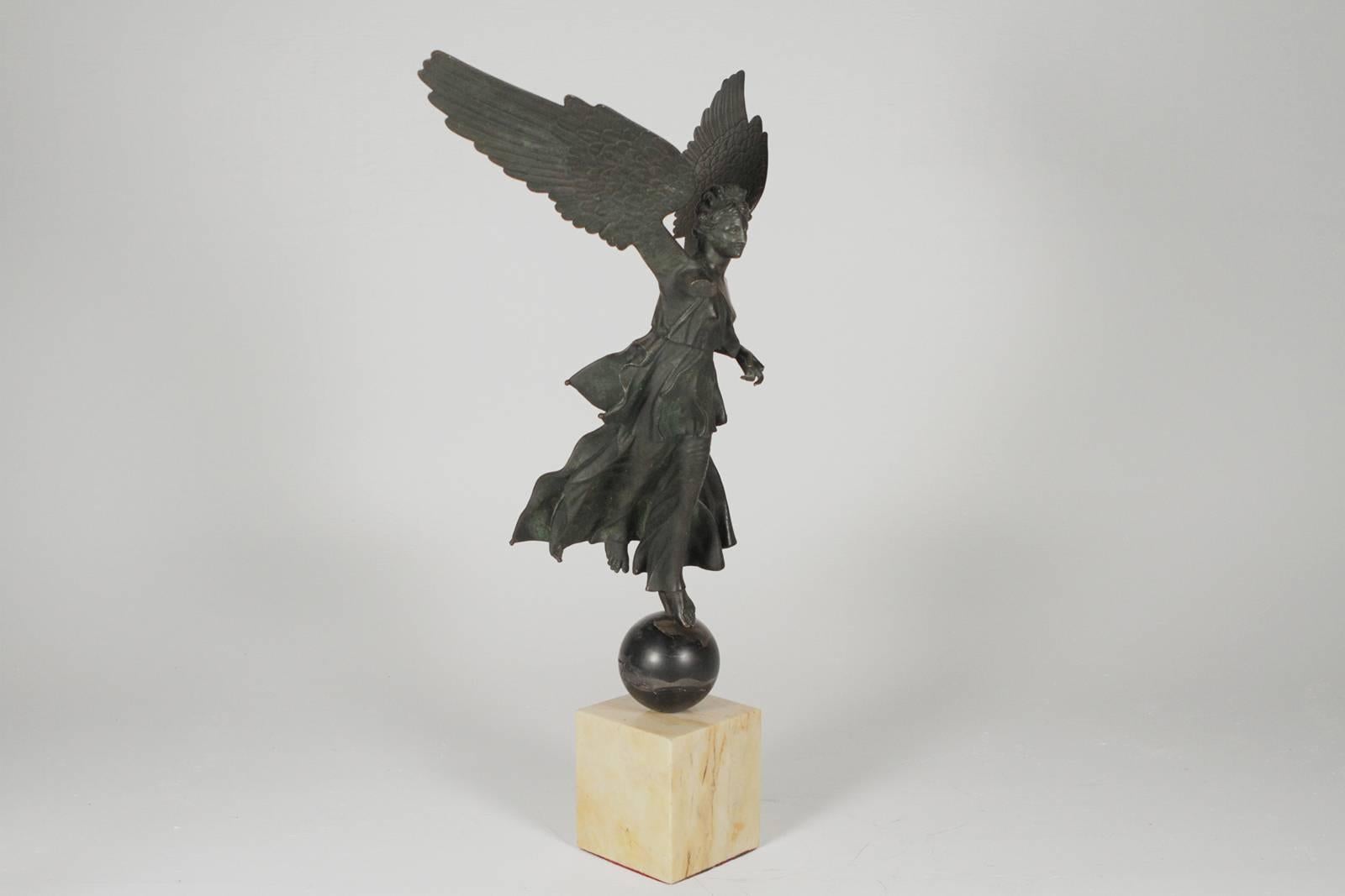 A bronze winged figure on a marble base. The original patinated finish with a weather finish. The female figure with an arm band with jewel cabochon.