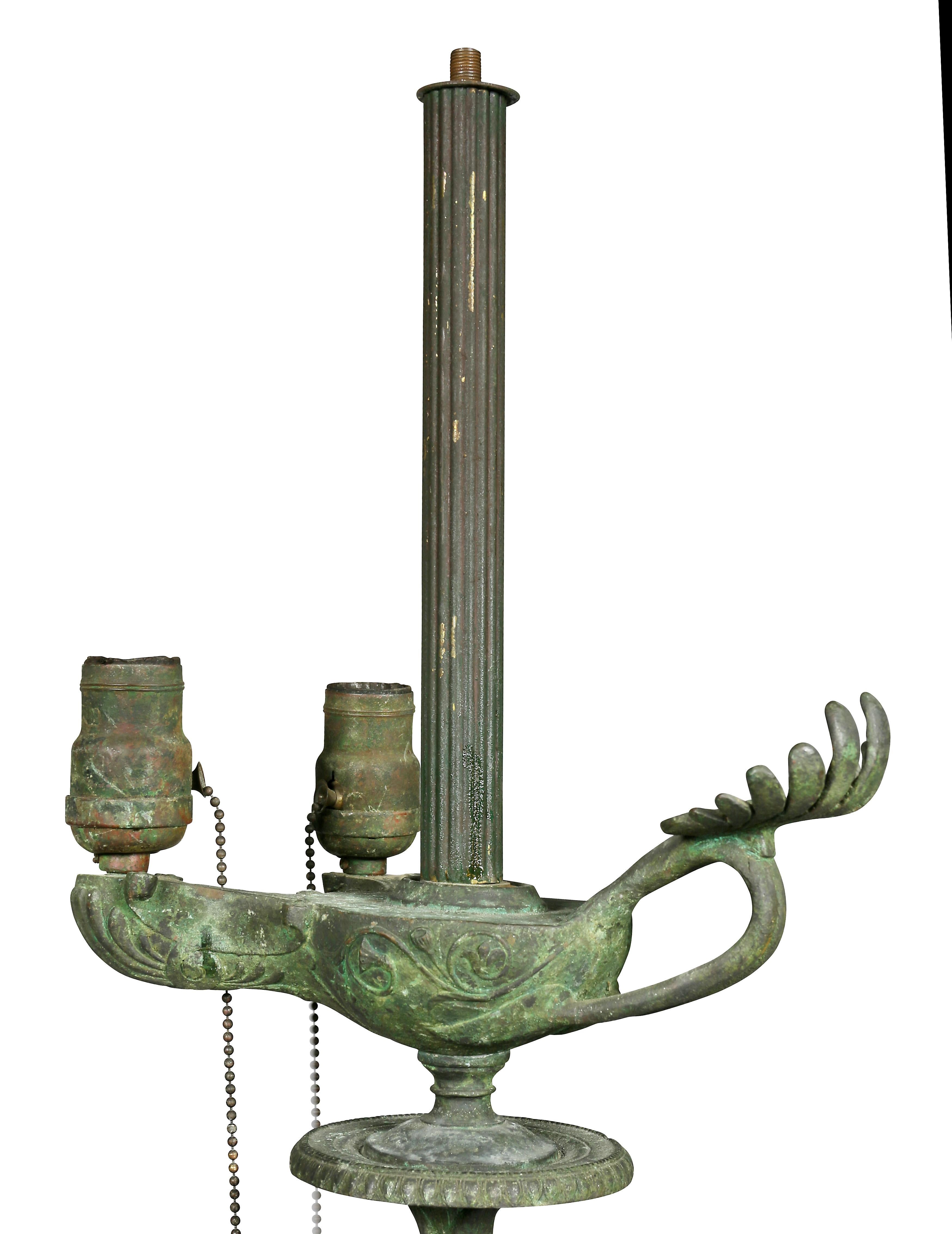 With vertigris patination imitating oxidation with an oil lamp with anthemium handle and two sockets over a winged figure of a woman, raised on tripartite legs and paw feet. Estate of architect John Volk, Palm Beach Florida.