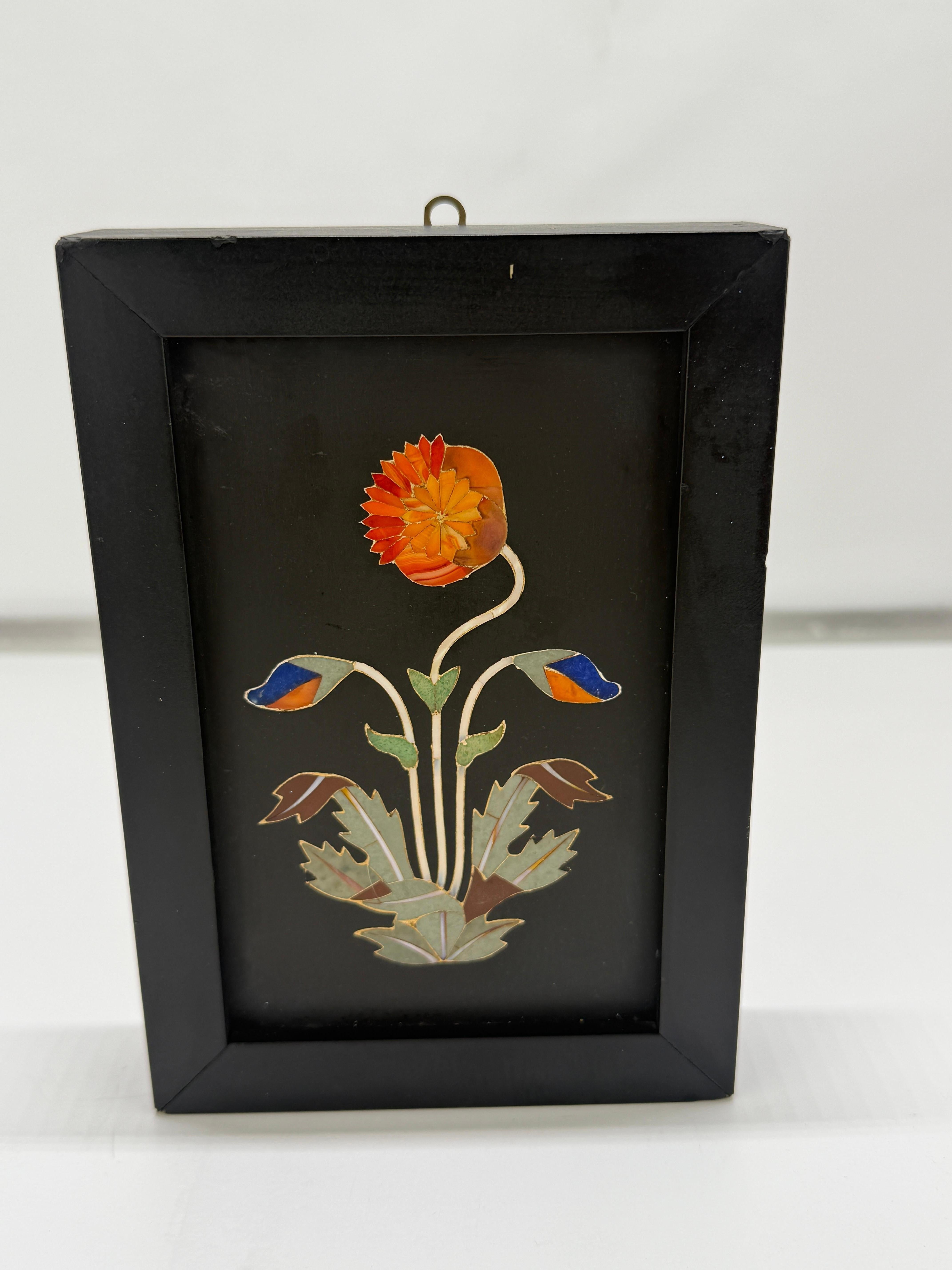 Un panneau raffiné en pierre dure pietra dura de Florentine datant du XIXe siècle, placé dans son cadre d'origine en bois ébonisé et conservant son anneau de suspension en laiton. La composition présente une étude botanique stylisée, magistralement
