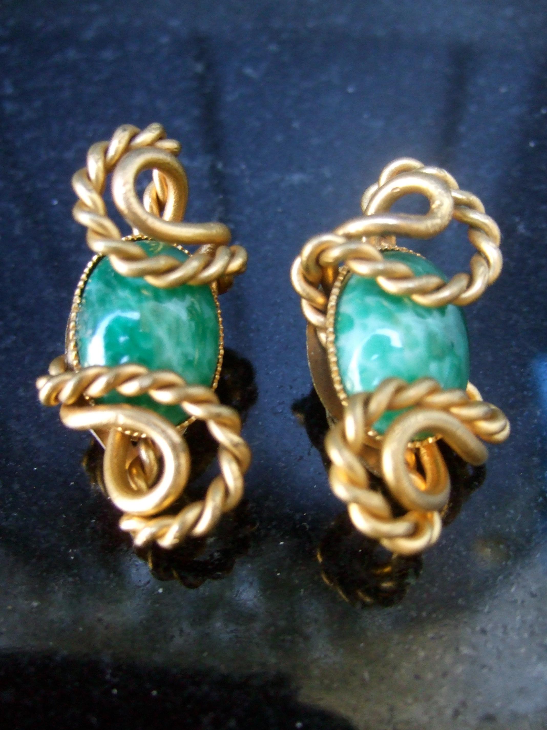 Pendientes de clip de piedra de cristal italiana diseñados por Silvana c 1970
Los elegantes pendientes están adornados con una piedra ovalada de cristal verde 
El cabujón ovalado de cristal está encerrado en sinuosas sinuosidades de metal dorado