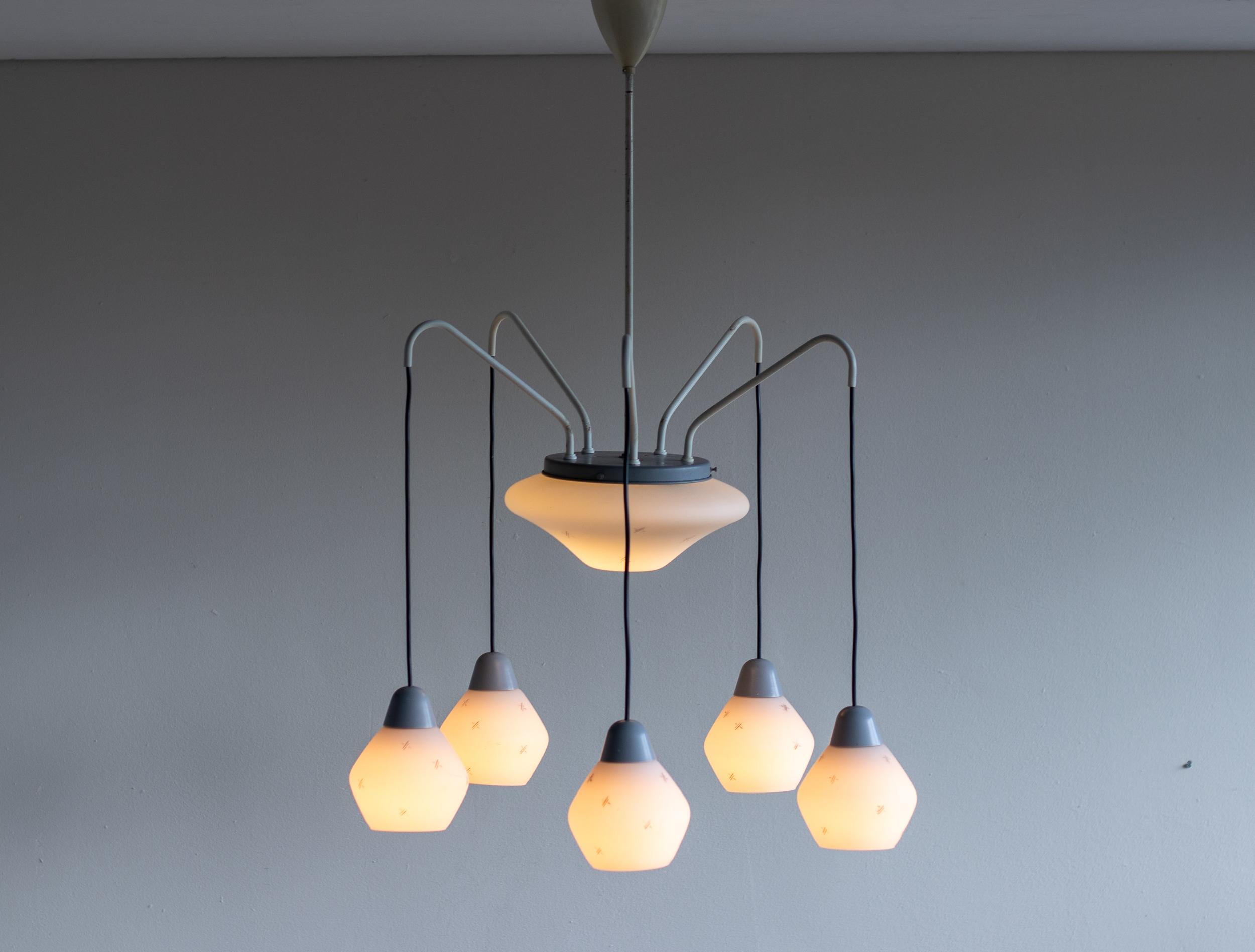 Magnifique lustre italien du début des années 1960, présentant une combinaison sophistiquée de laiton émaillé gris et de pampilles en verre dépoli aux formes élégantes. Ce luminaire raffiné comprend cinq abat-jour en verre suspendus, disposés autour