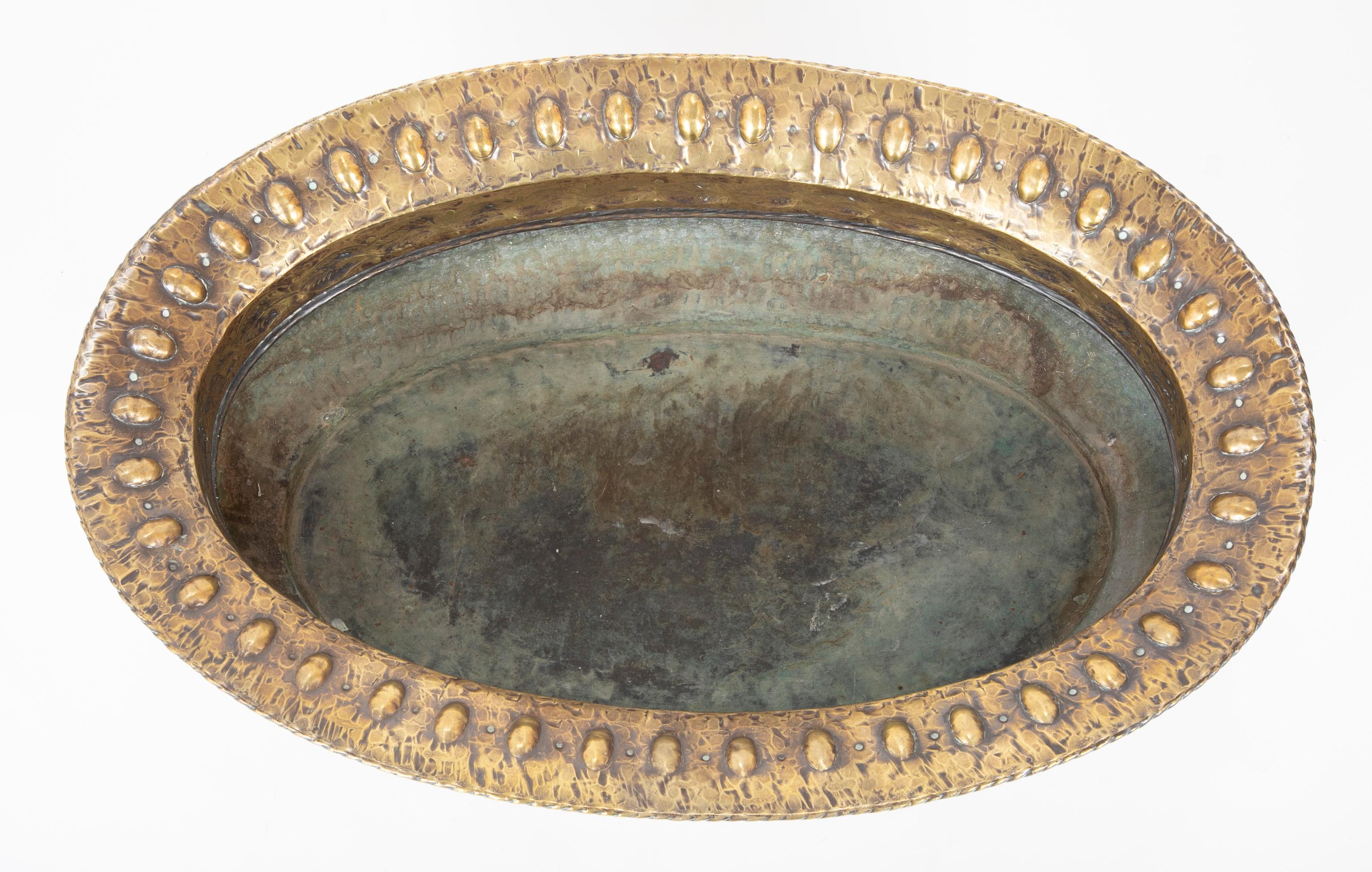 Impressive brass repousse Italian centerpiece with hand-hammered surface. The rim decorated with raised oval cabochons, the band underneath with etched interlocking leaves, the body with a stippled rusticated surface. Supported on four lion paw