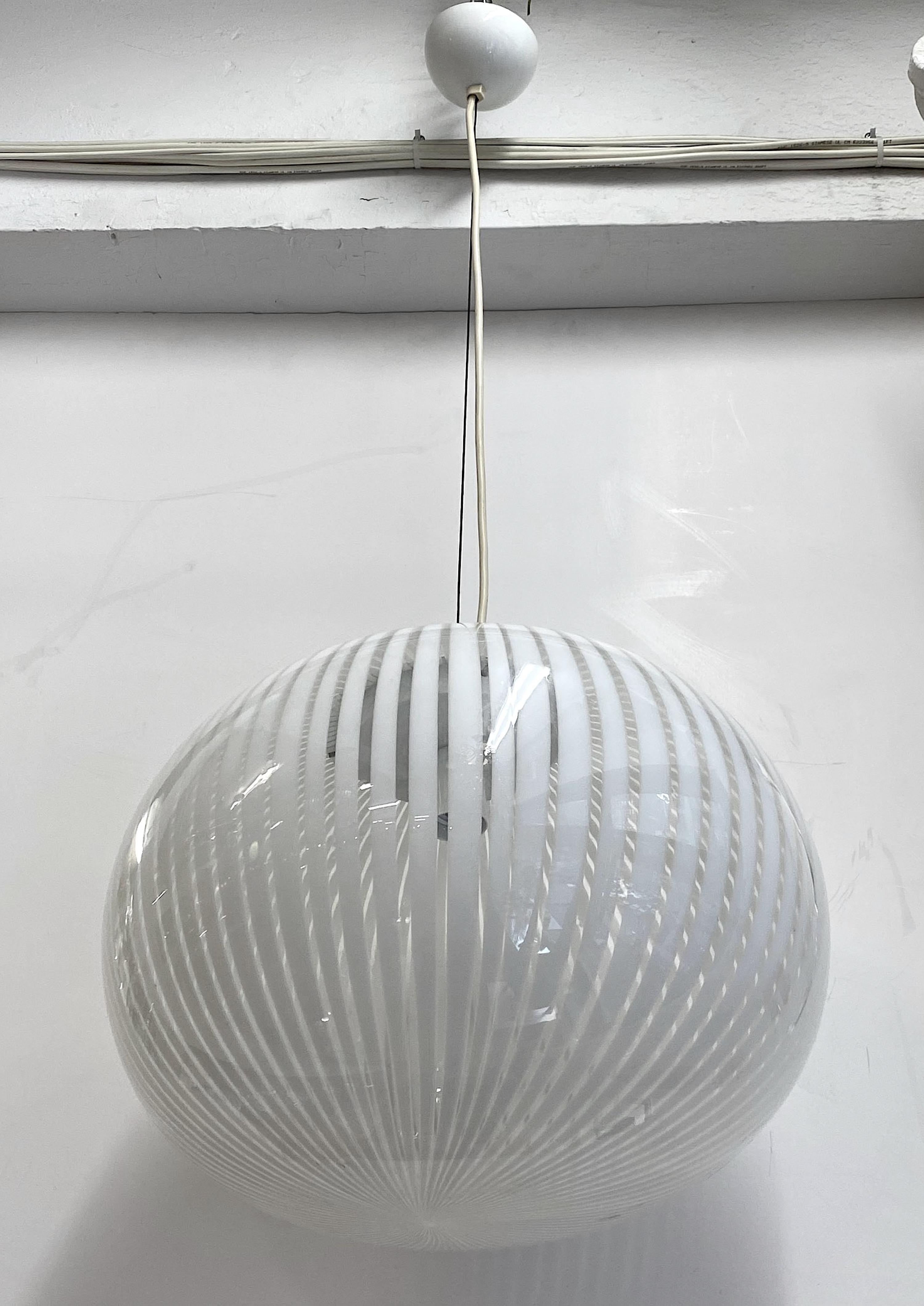 A wonderful 1970s Italian stripe glass pendant light from Murano, Italy. The hand blown globe in clear and white stripe glass houses a single standard socket. The glass globe is slightly flattened and not a perfect sphere intentionally. It measures