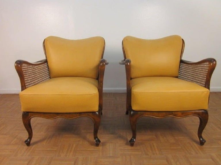 Italian hand-caned leather armchairs in the style of Paolo Buffa. The chairs have solid walnut frames with caned sides and backs, cushioned seat and back with yellowish-gold leather upholstery.