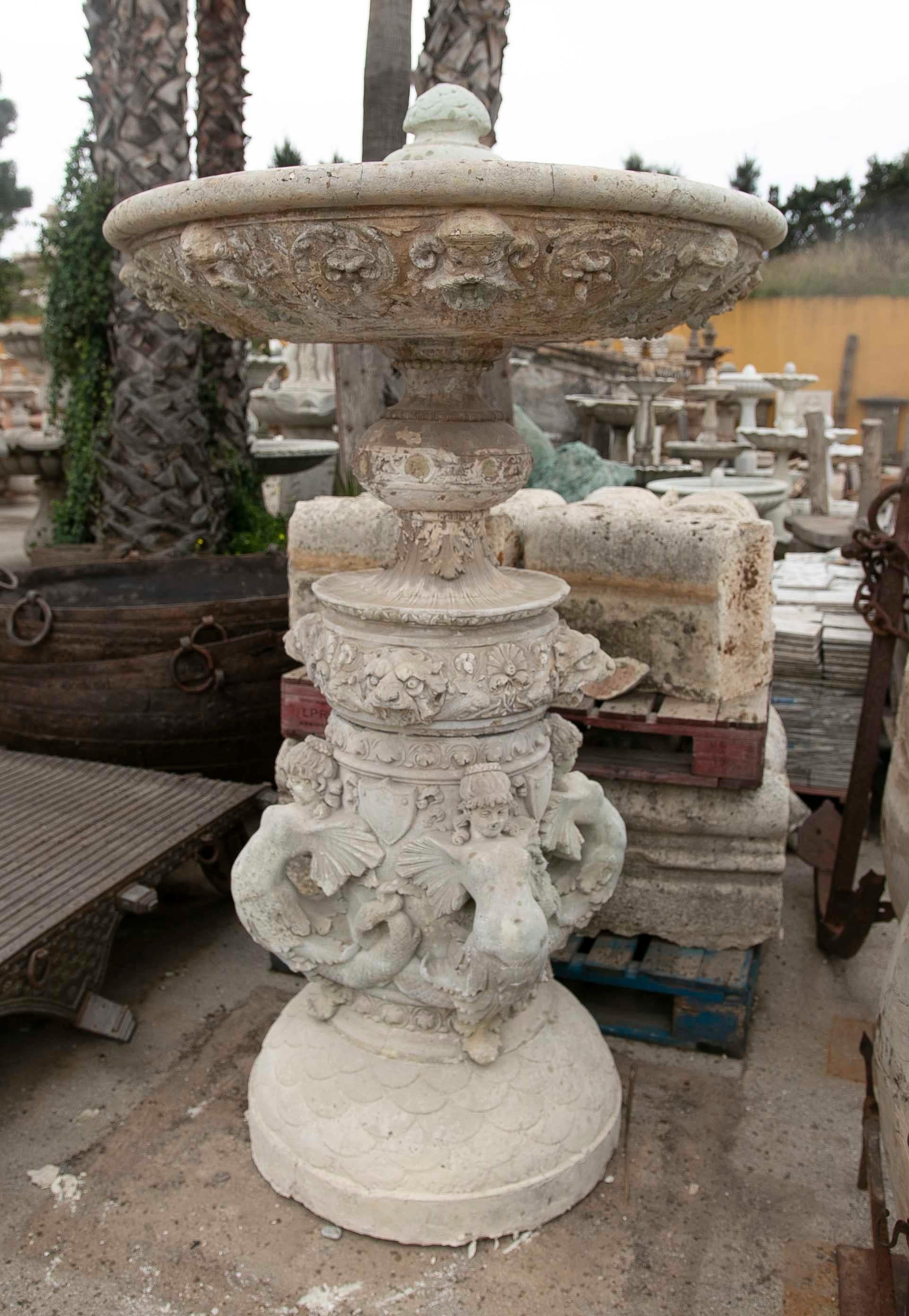 A hand-carved stone centre fountain decorated with fantastic animals and plant scrolls on the upper plate, in the centre we can see the decoration of a family coat of arms and more plant motifs, the lower part decorated with women with fishes on the
