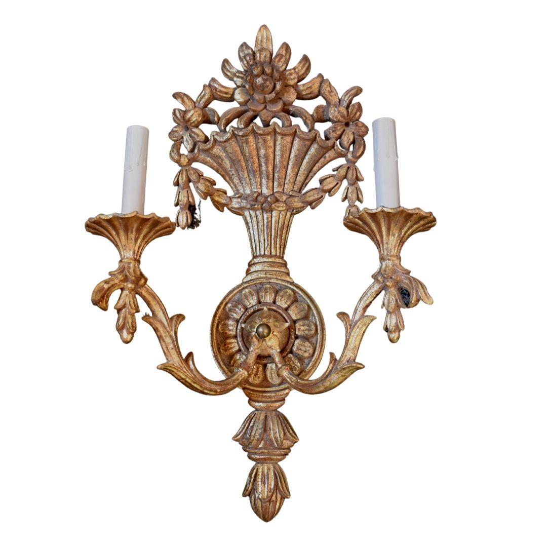Italian hand carved wood sconces, gilt. Marked Made in Italy, 2 candle sockets per sconce, urn style detail with flowers, gold distressed paint, gold swag of leaves, leaf and scroll detailing on the arms. 22