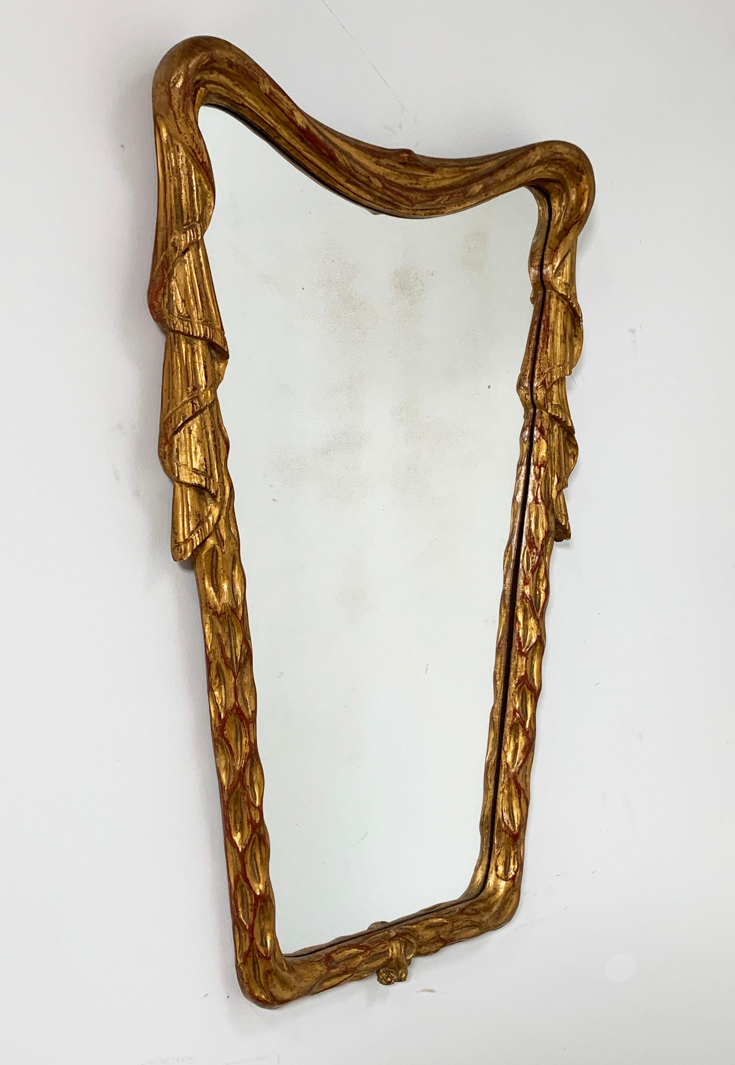 A dramatic Italian hand carved and giltwood mirror of draped trapezoidal form, circa 1930s. Measures: 21.75” wide x 33” long.