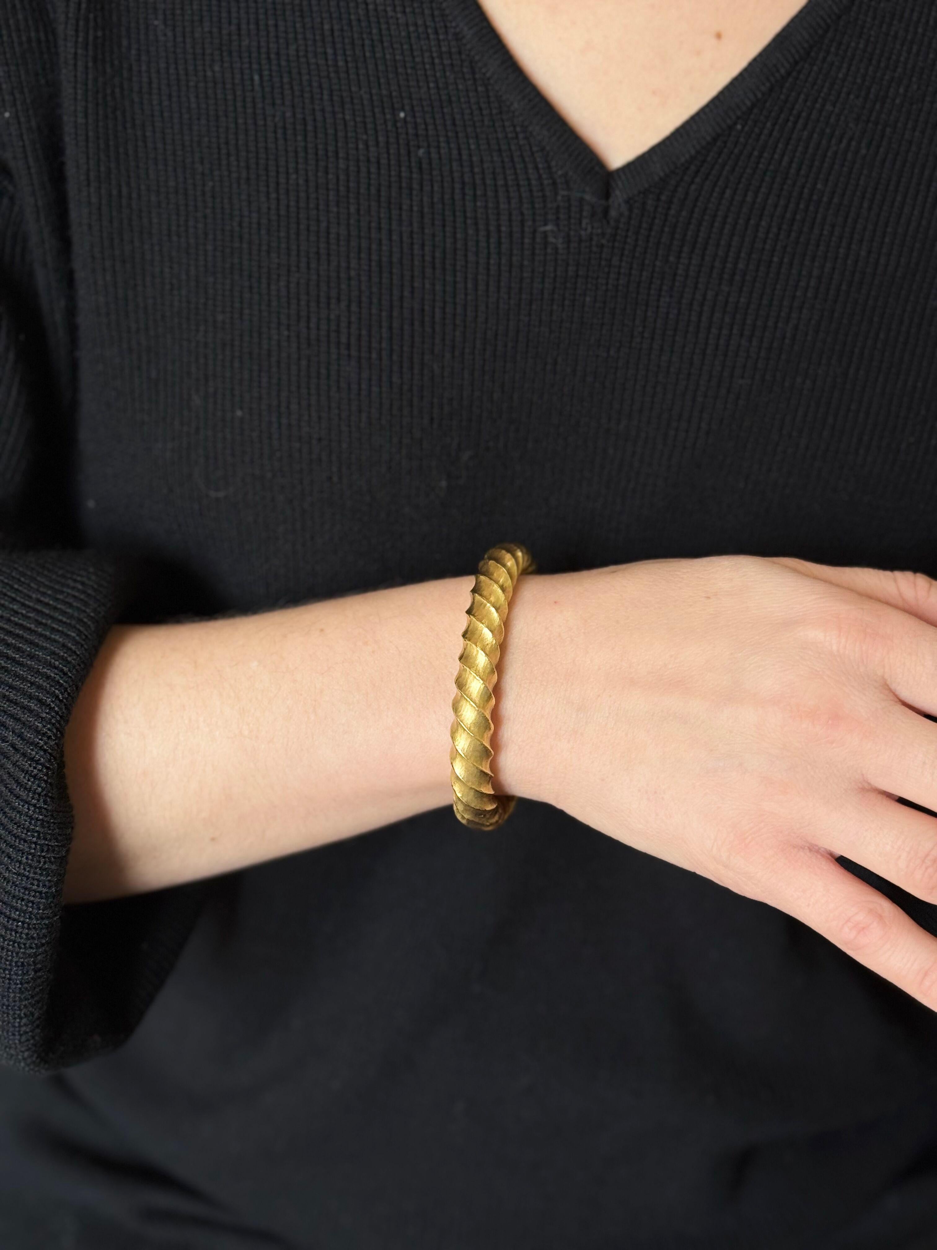 Bracelet bangle de fabrication italienne, serti en or jaune 18k, finition martelée à la main, design torsadé. Le bracelet s'adapte à un poignet d'environ 7