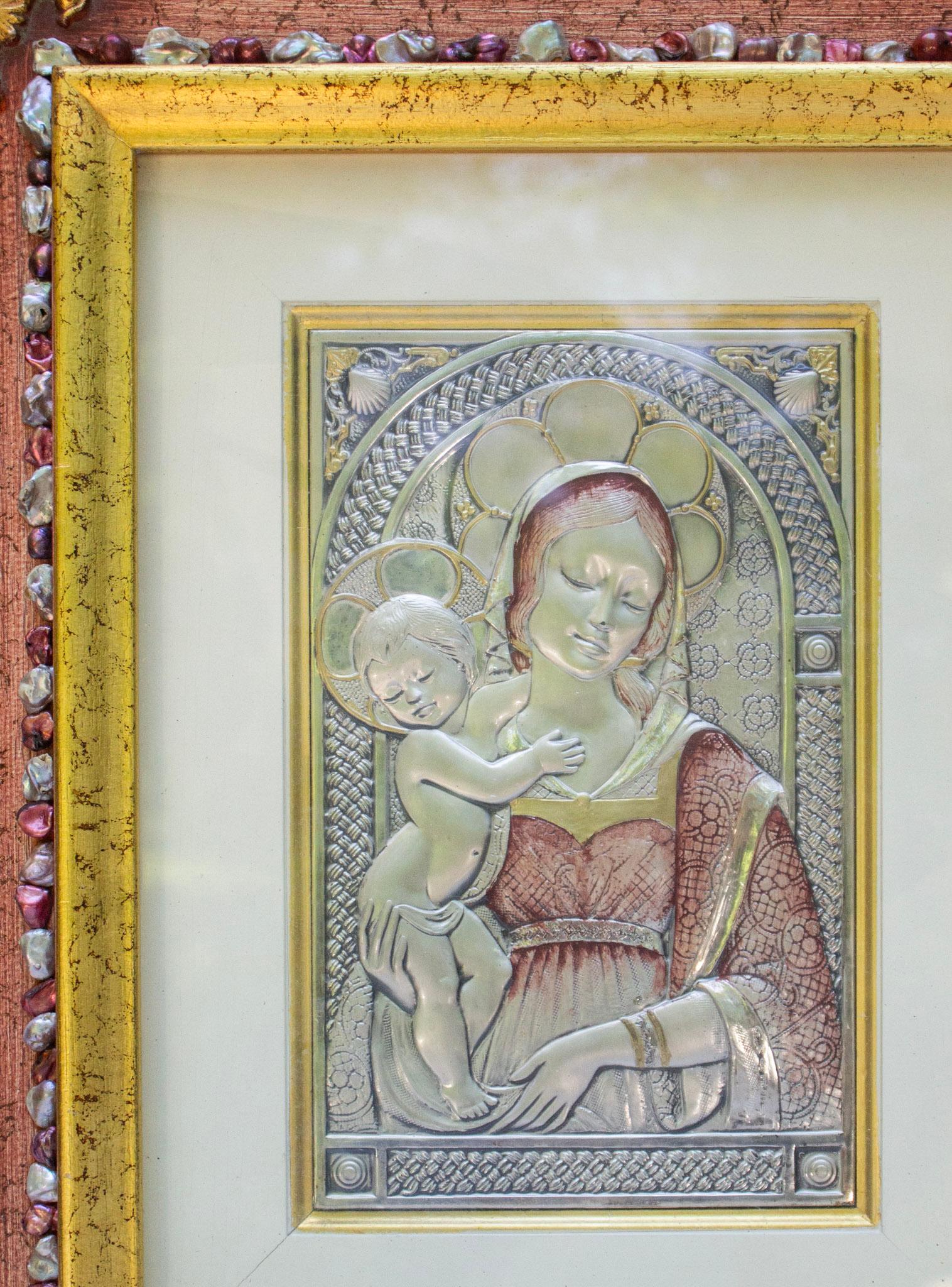Vierge à l'enfant italienne en argent martelé à la main provenant de Sicile, détaillée avec des teintes dorées et rouge-vin clair, s'harmonisant parfaitement avec le cadre original en bois sicilien. Le cadre intérieur est bordé de perles baroques
