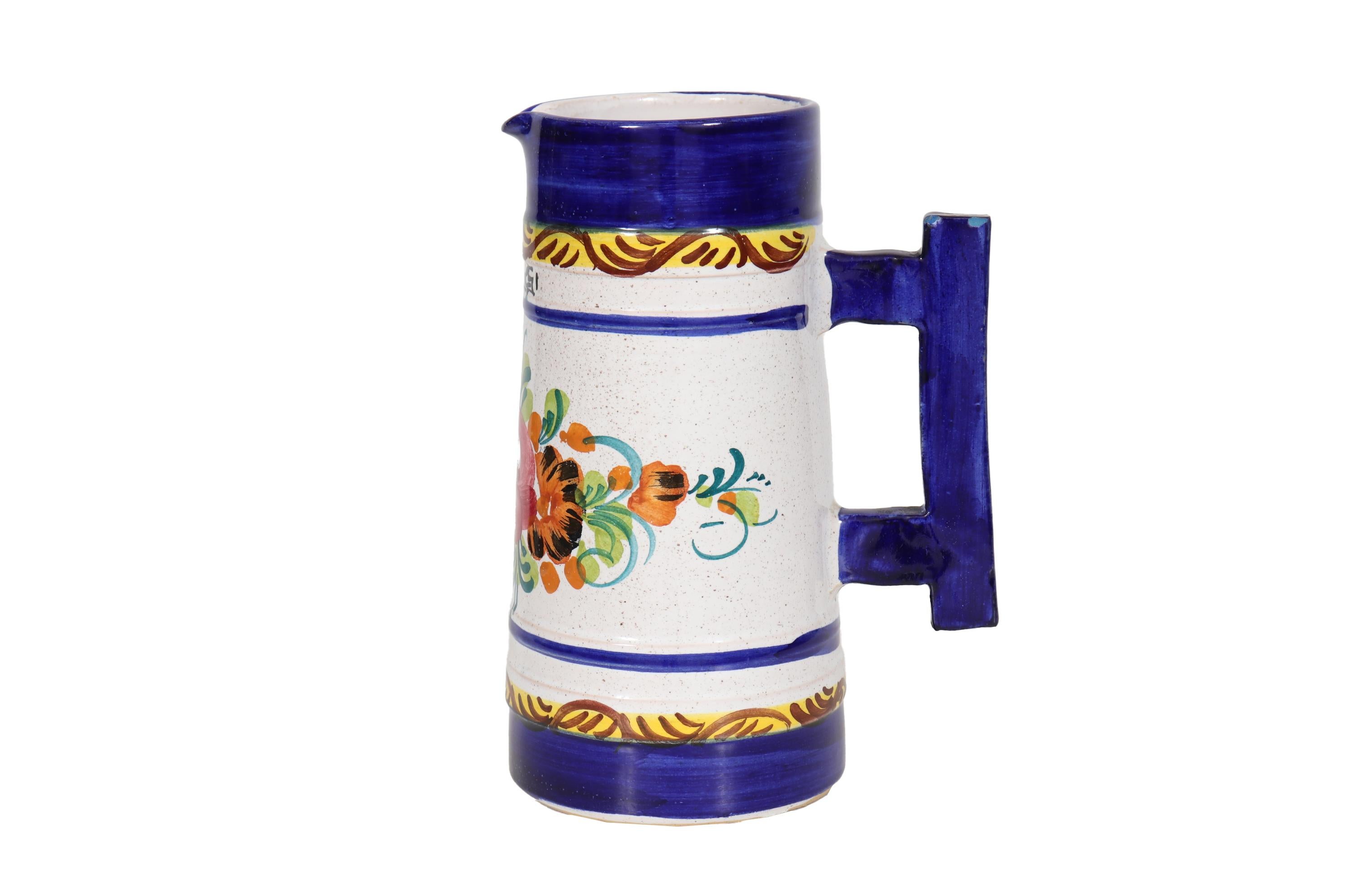 An Italian ceramic pitcher. Hand painted with a colorful floral spray on a white background, framed in rich cobalt blue. In the front it’s signed “Fiuggi”, an Italian province. In the back is a squared handle.