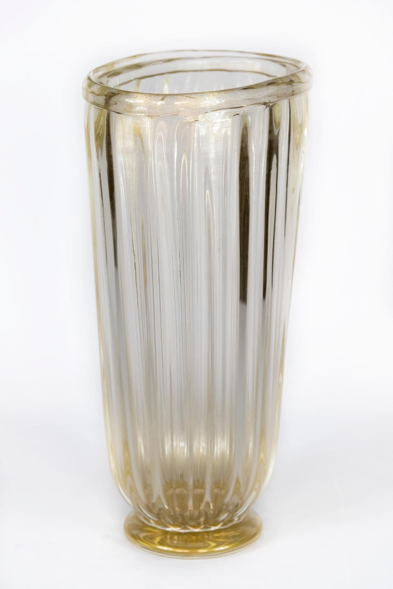 Ce vase de forme assymétrique/ovale, fabriqué à la main en Italie, est en verre de Murano transparent avec de la poussière d'or incrustée.
 