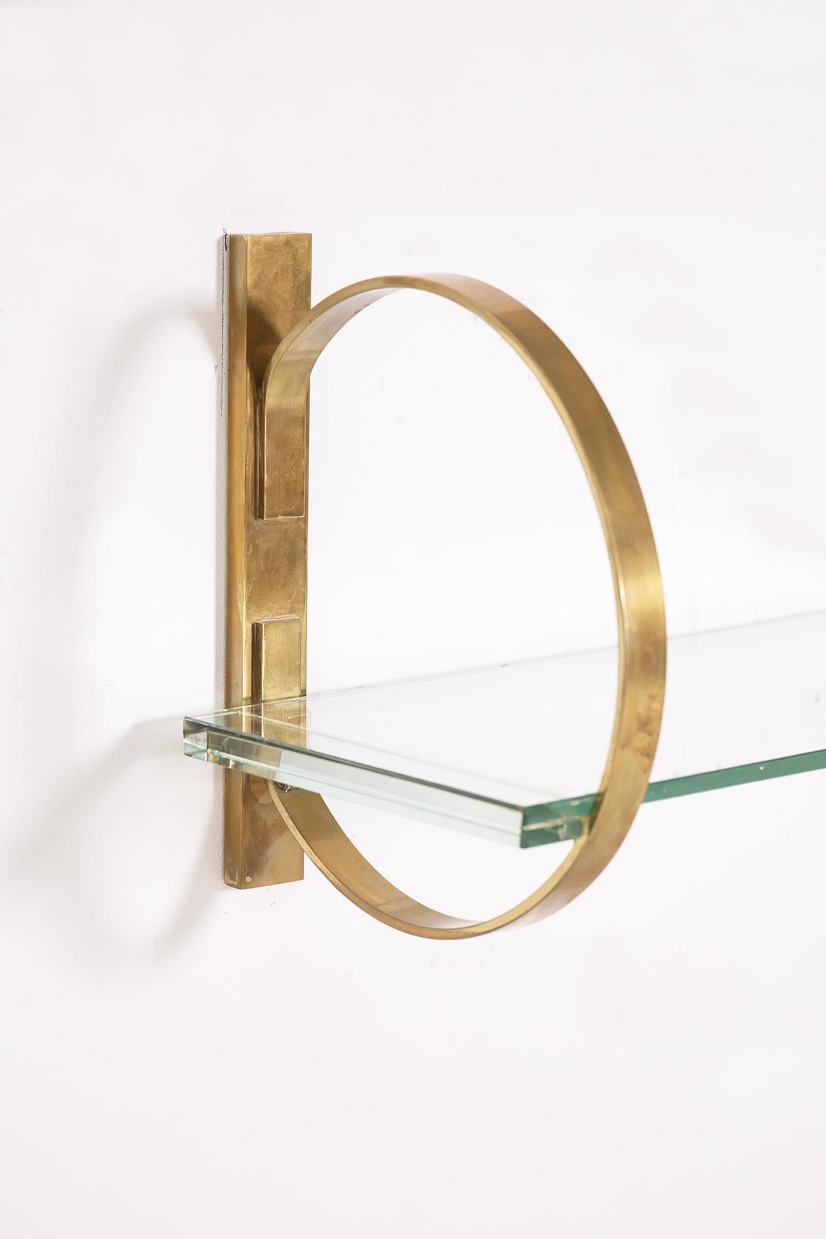 Italian hanging console table from the 1960s. The console is made with a thick glass top of the period, transparent in colour tending to green.
The glass top is supported by two circular brass brackets, anchored to the wall. The brass has a