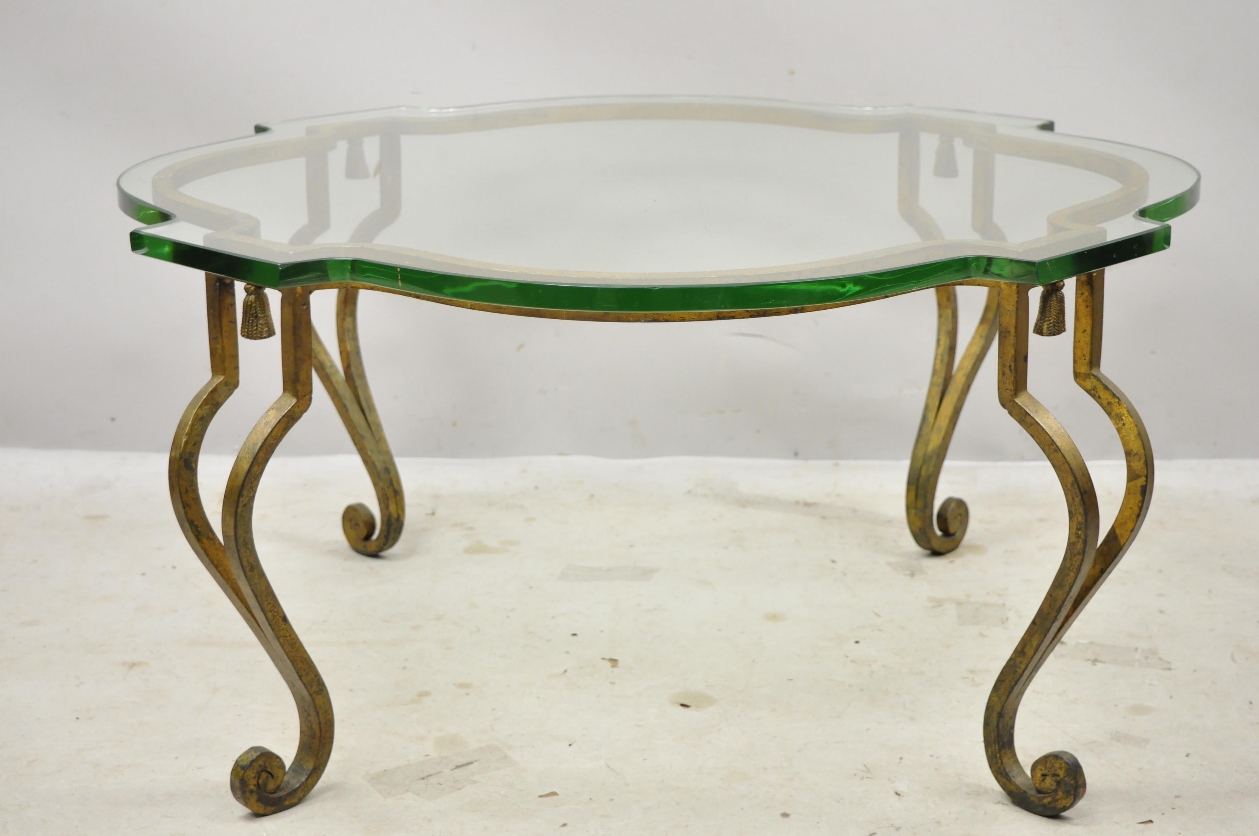 Italian Hollywood Regency distressed gold gilt iron scalloped glass coffee table. Item features heavy iron scrollwork base with tassels, thick scalloped shaped glass top, distressed gold finish, cabriole legs, very nice antique item, great style and