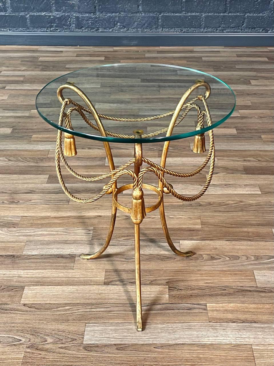 Condition: Original Vintage Condition
Materials: Gilt-Metal, Original Glass Top

This Italian Hollywood Regency side table, crafted in the 1960s, exudes timeless glamour with its gilt-metal rope and tassel design supporting the original round glass