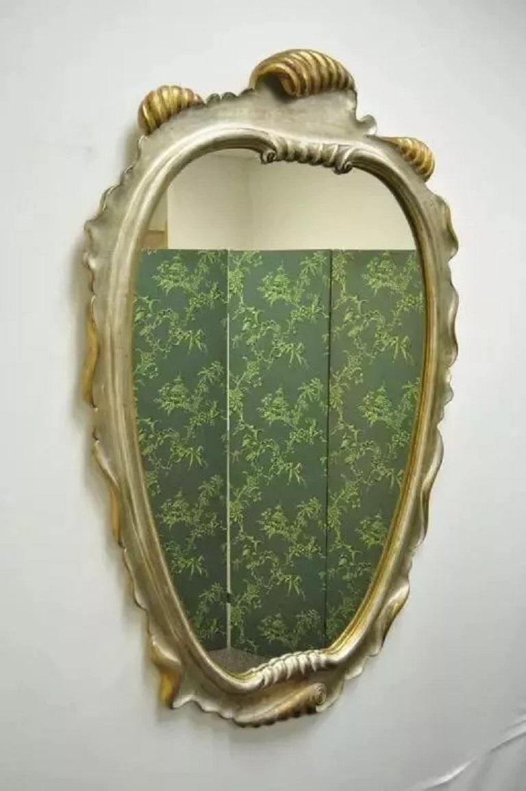 Vintage Italian Hollywood Regency Gold and Silver Giltwood Scroll Carved Wall Mirror. Ce superbe miroir vintage présente un cadre en bois sculpté de festons avec une finition argentée et dorée attrayante et originale. Circa Mid 20th Century.