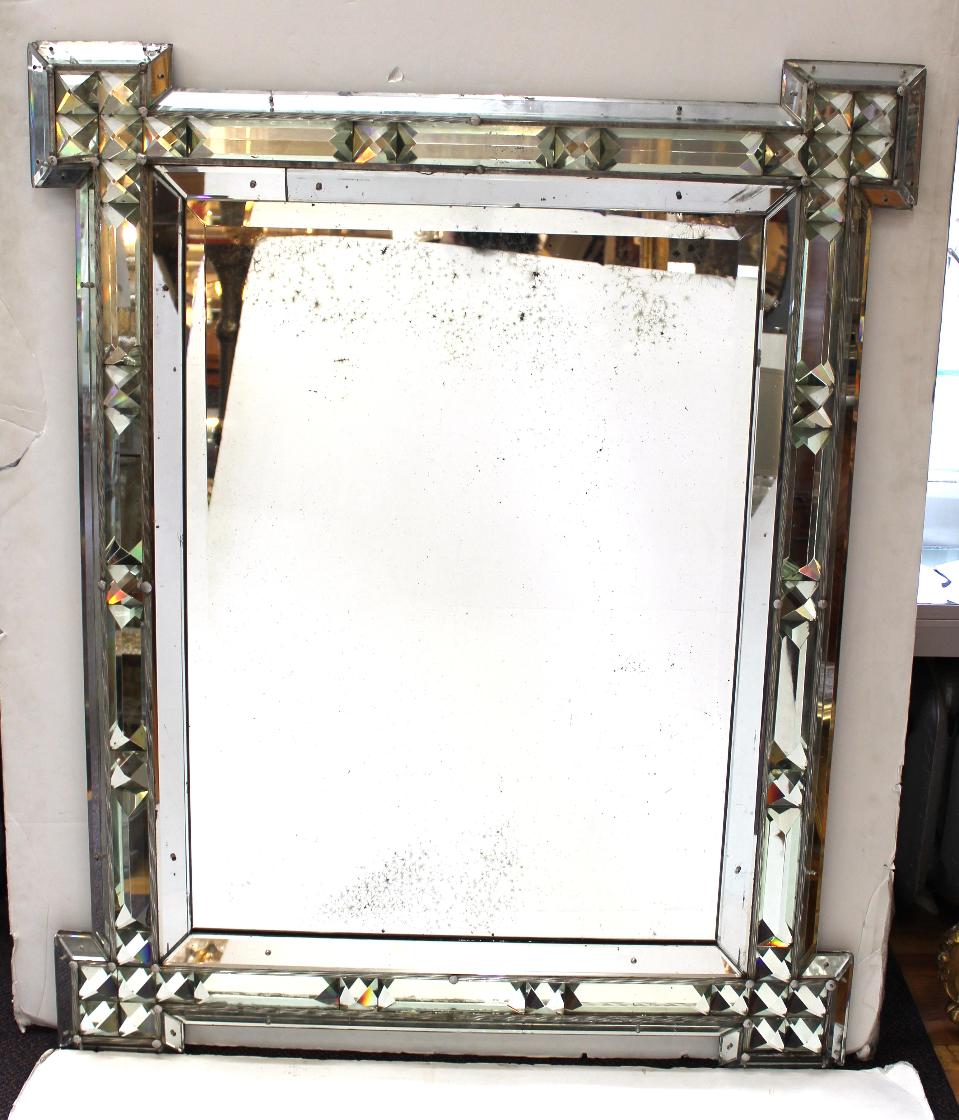 Hollywood Regency mirror with a decorative border inset with cut-glass prisms and twisted blown glass baguettes. The piece was made in Italy in the mid-20th century and has wear to the mirror, some replaced border elements and tarnish. Overall in