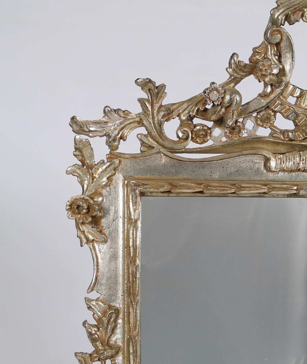 Italian Hollywood Regency mirror made of carved wood with silver leaf. The mirror features intricate carved scroll work with flowers and fruits. Wear appropriate to age and use. The mirror remains in excellent vintage condition.