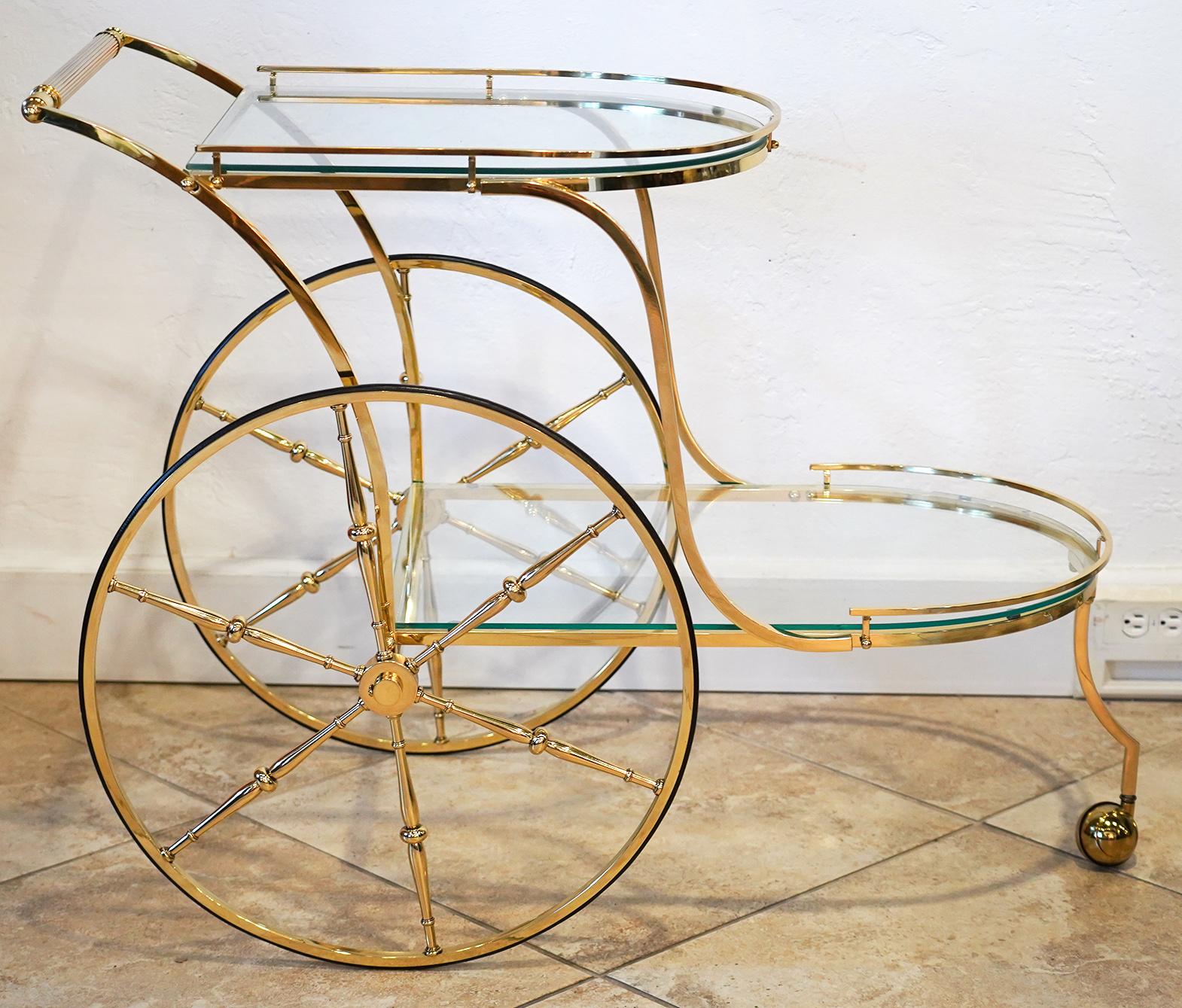 This artfully crafted vintage brass bar cart with two galleried glass levels feature two large wheels and one front coaster. It is an elegant design with lots of space for large bottles and accessories.