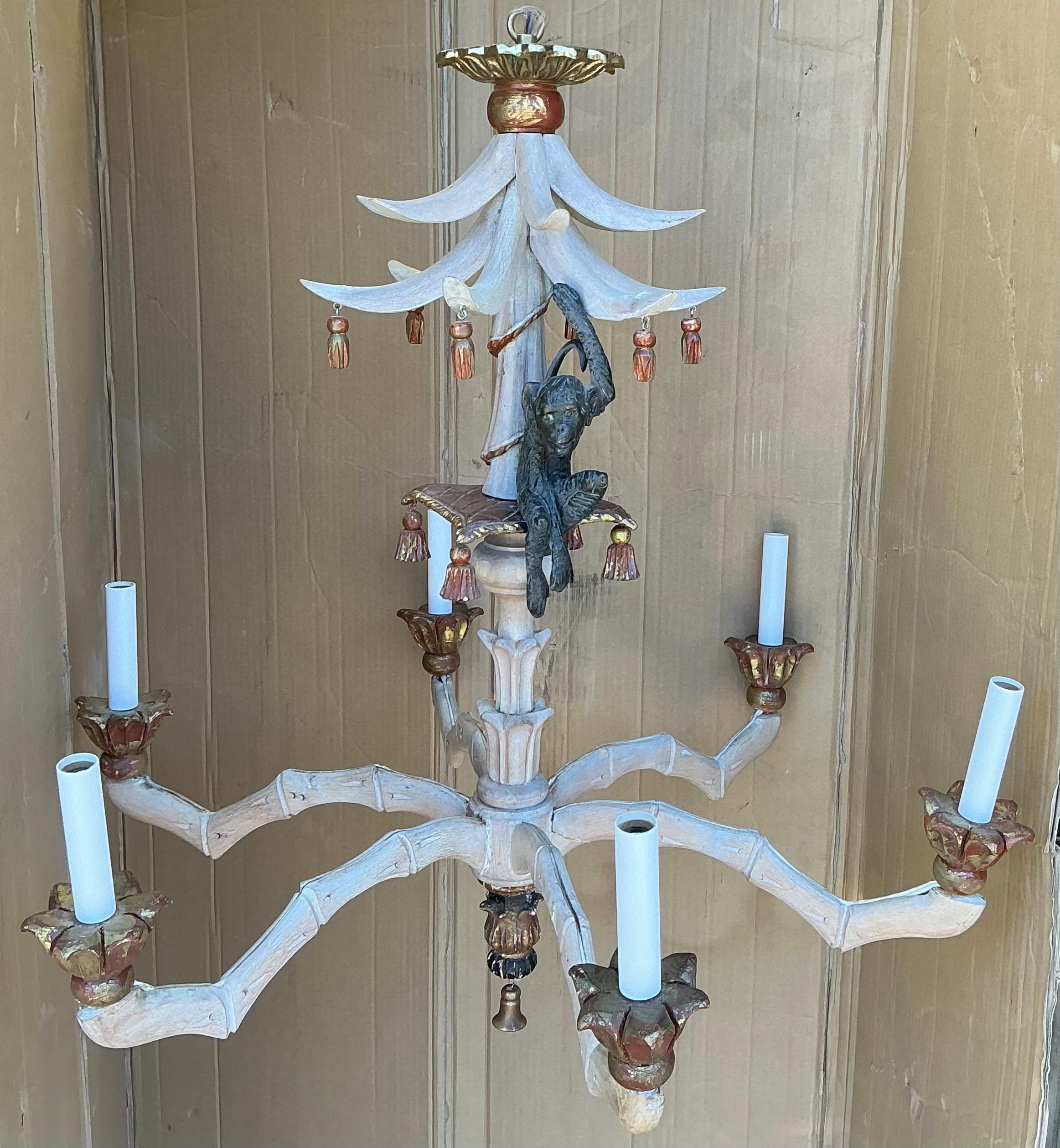This is a Hollywood Regency / Chippendale Style carved faux bamboo chandelier with a seated monkey. The palm fronds come together to form an illusion of a pagoda giving the piece a chinoiserie feeling to it. There are six arms, and the wiring is