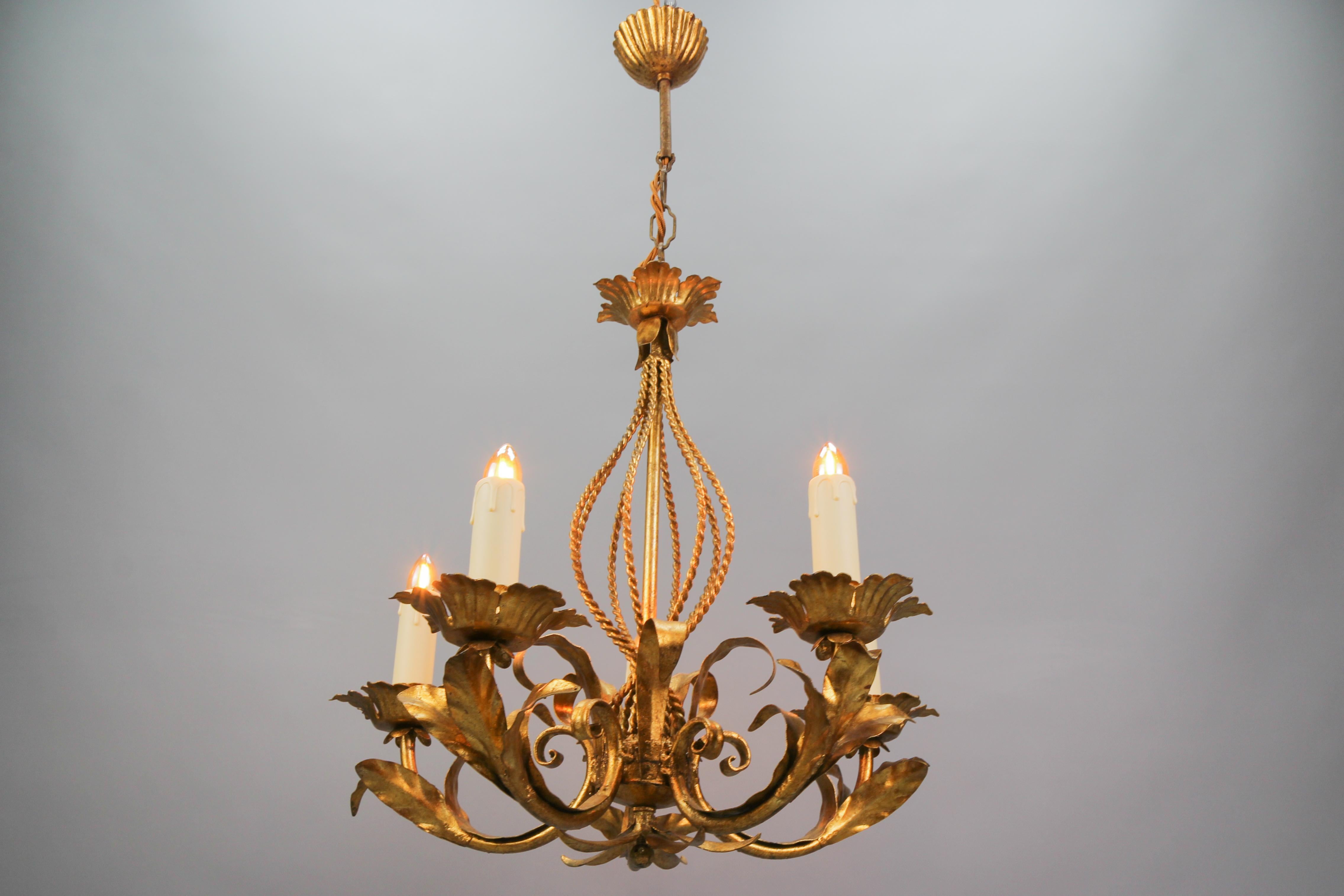 Italian Hollywood Regency style gilt metal five-light chandelier, circa the 1970s
A beautiful Italian gilt metal/toleware five-light chandelier from the circa 1970s. The golden light fixture is adorned with leaves and beautifully shaped ropes on